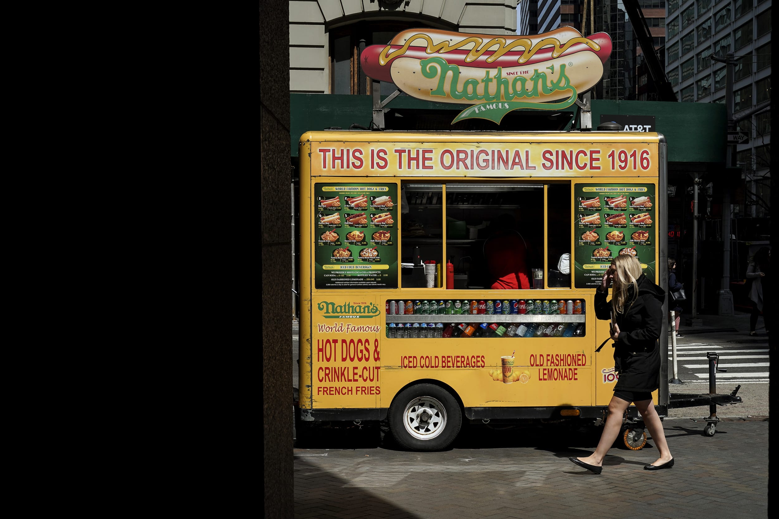 Image: A woman walks past a Nathan's hot dog cart on Wall Street in New York on April 12, 2019.