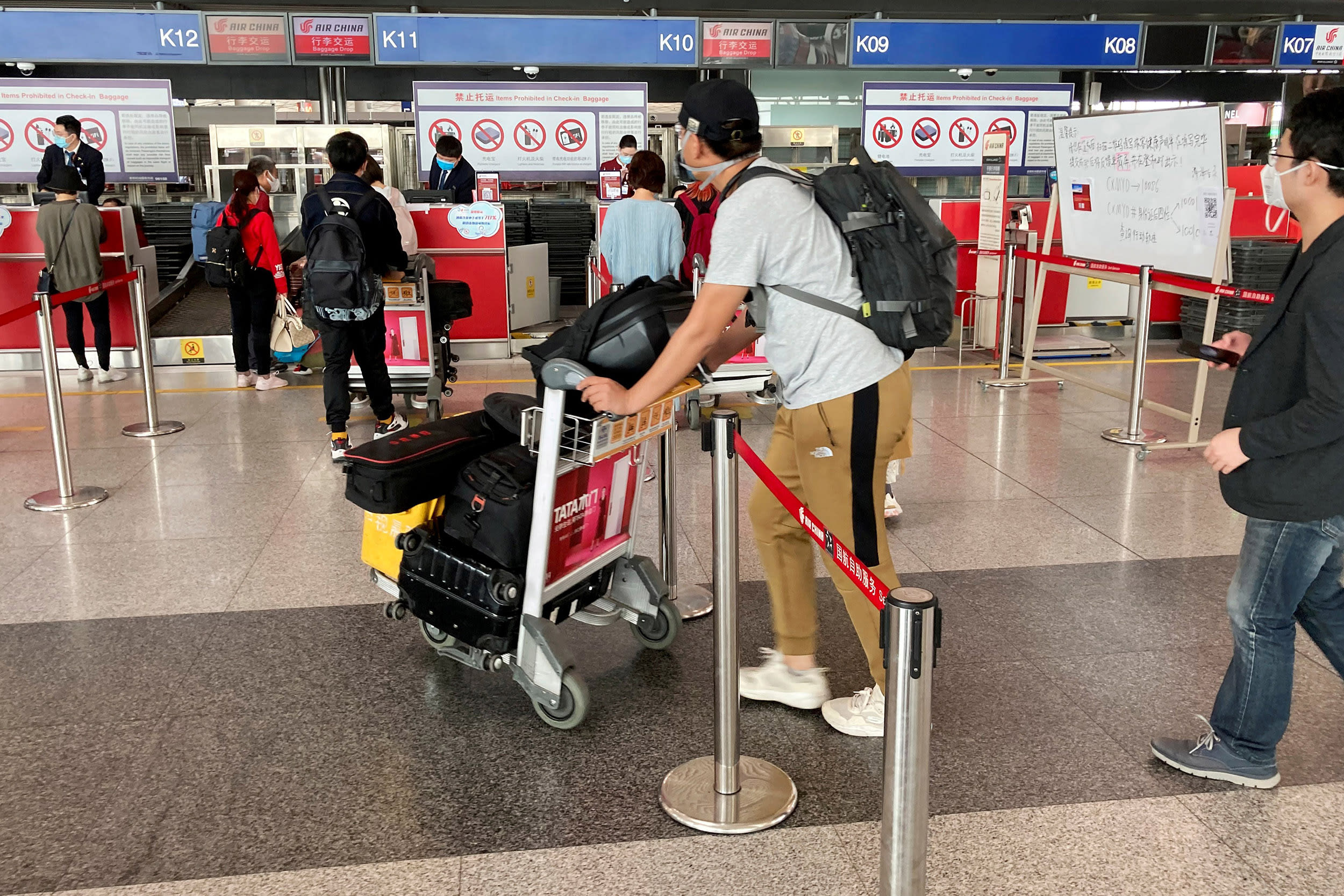 Image: Travelers wear face masks while waiting to check in at the Beijing Capital International Airport on Thursday.