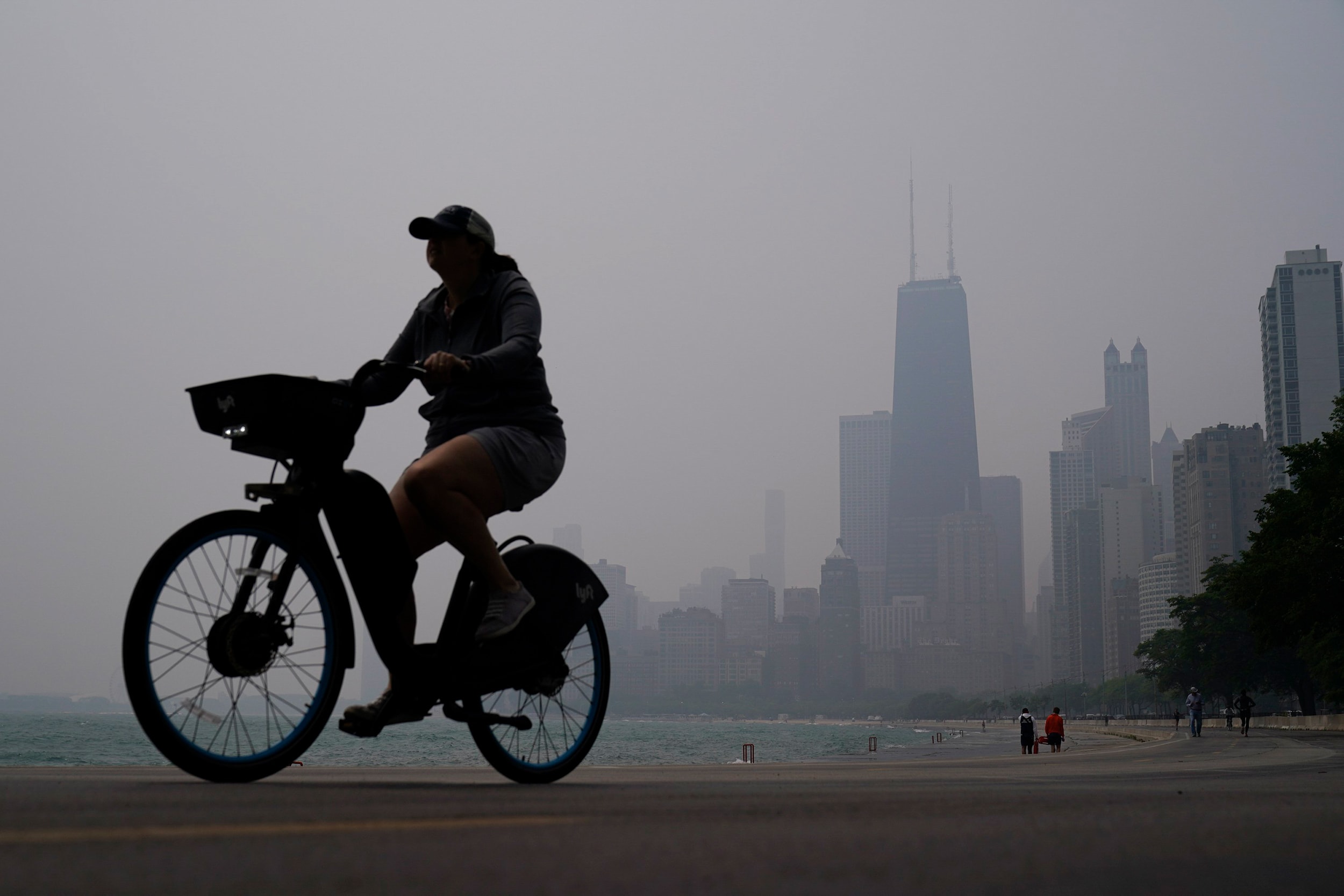 A person rides a bicycle along the shore of Lake Michigan as the downtown skyline is blanketed in haze from Canadian wildfires Tuesday, June 27, 2023, in Chicago.