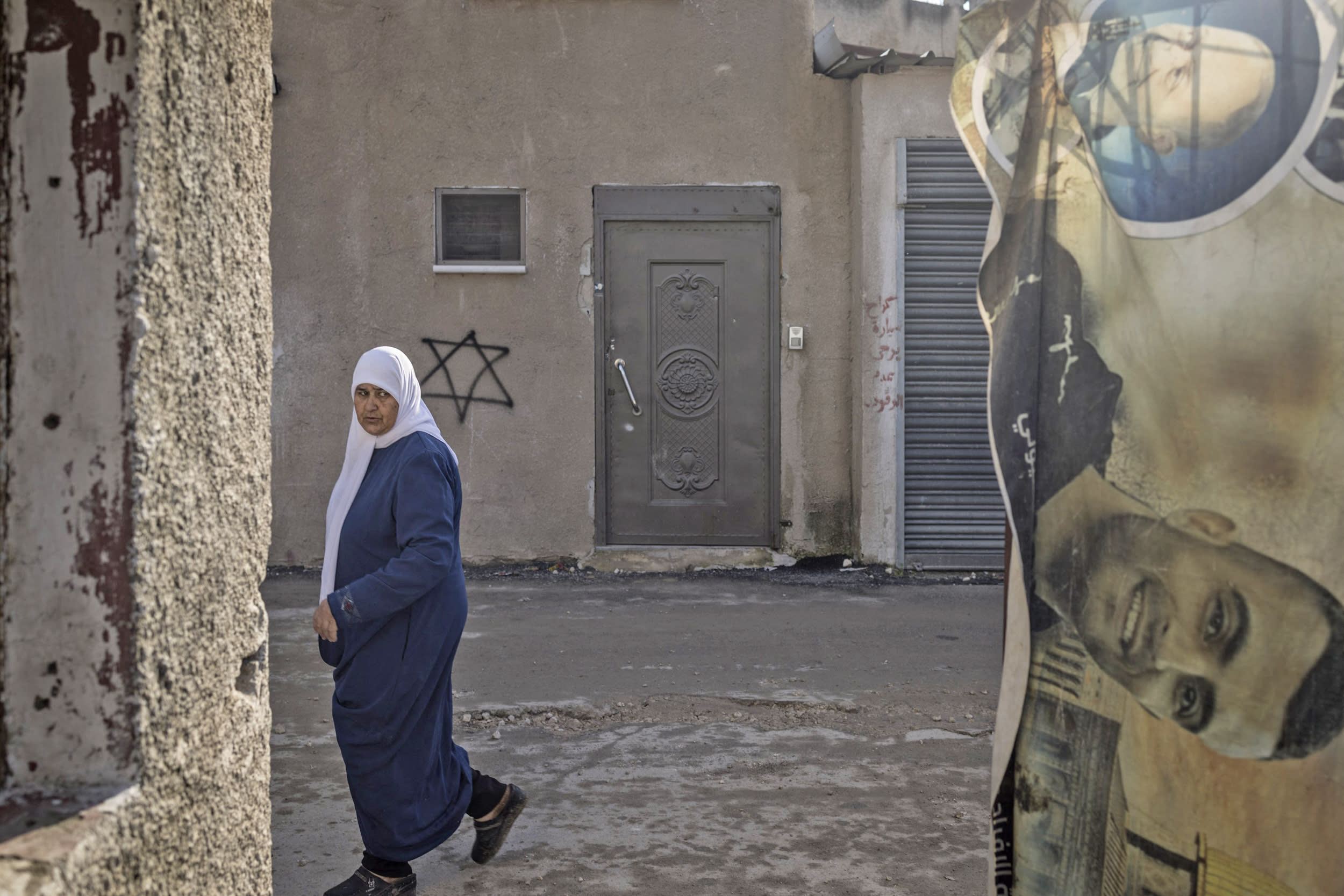A woman looks at a poster of a Palestinian man killed in a previous Israeli army operation as she walks past a Star of David spray-painted on the wall of a house in the Jenin refugee camp in the occupied West Bank on Dec. 14, 2023. 