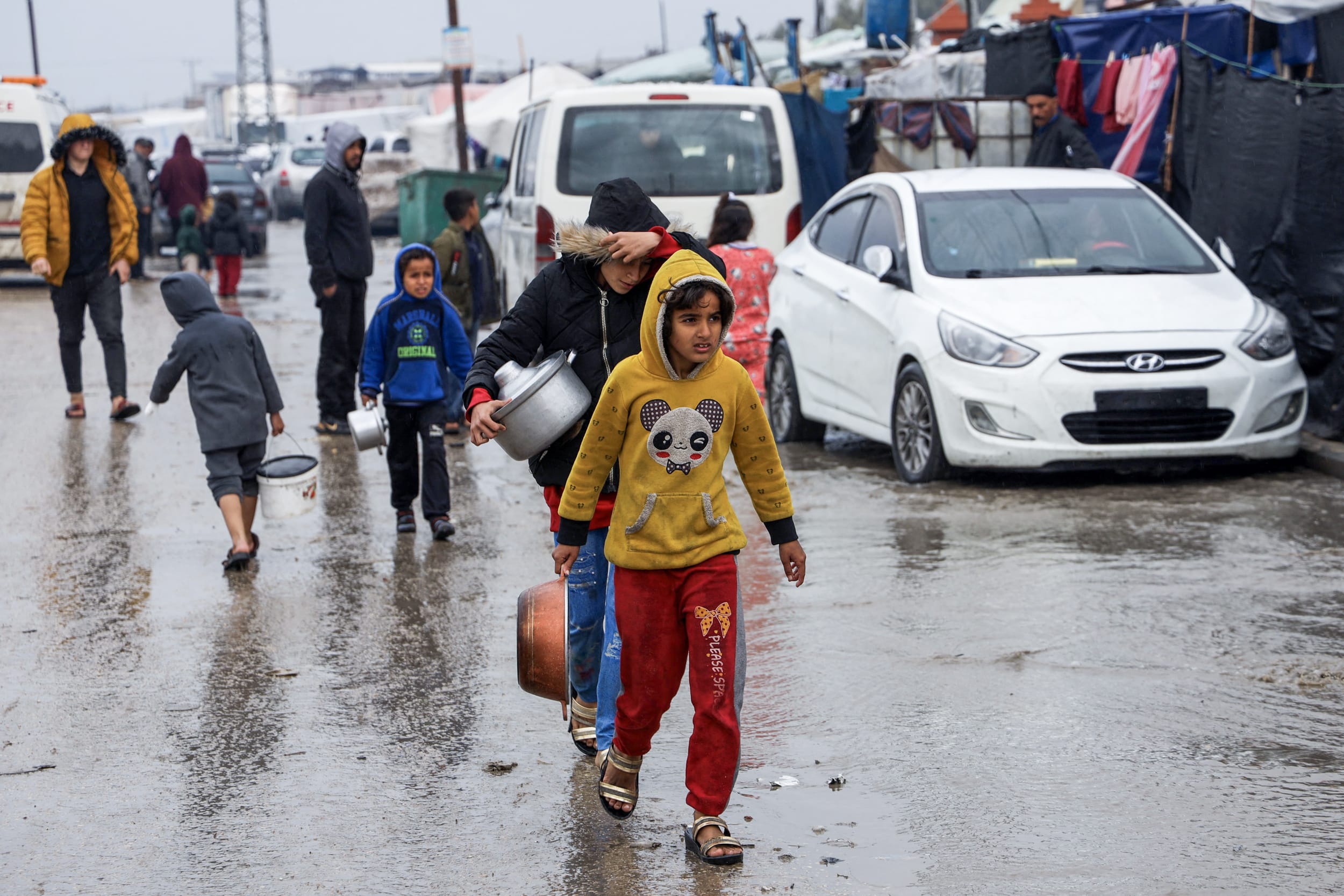 Displaced Palestinians walk through raiy weather and flooded streets to get food rations at a makeshift tent camp in Rafah in the southern Gaza Strip on Feb. 2, 2024.