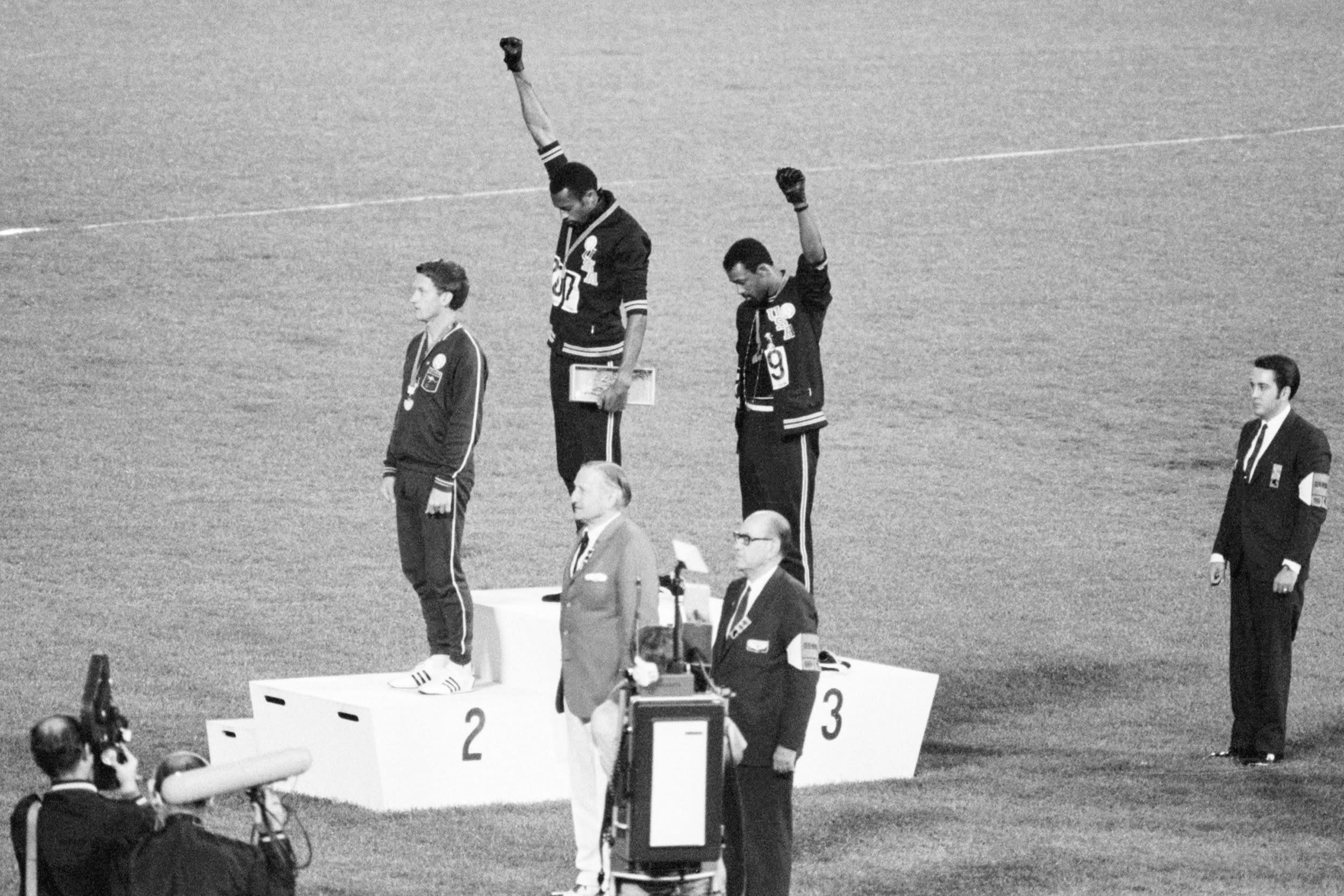 With heads lowered and black-gloved fists raised in the black power salute, they refuse to recognize the American flag and national anthem. Australian Peter Norman is the silver medalist.