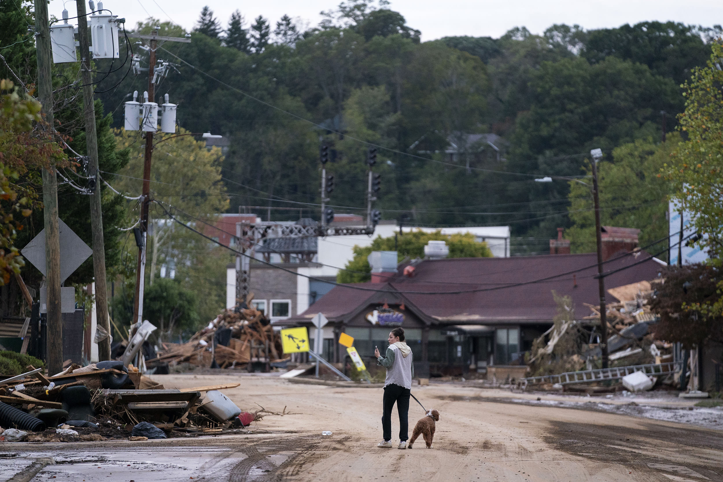 A woman walks her dog past debris from Hurricane Helene in Asheville, N.C.