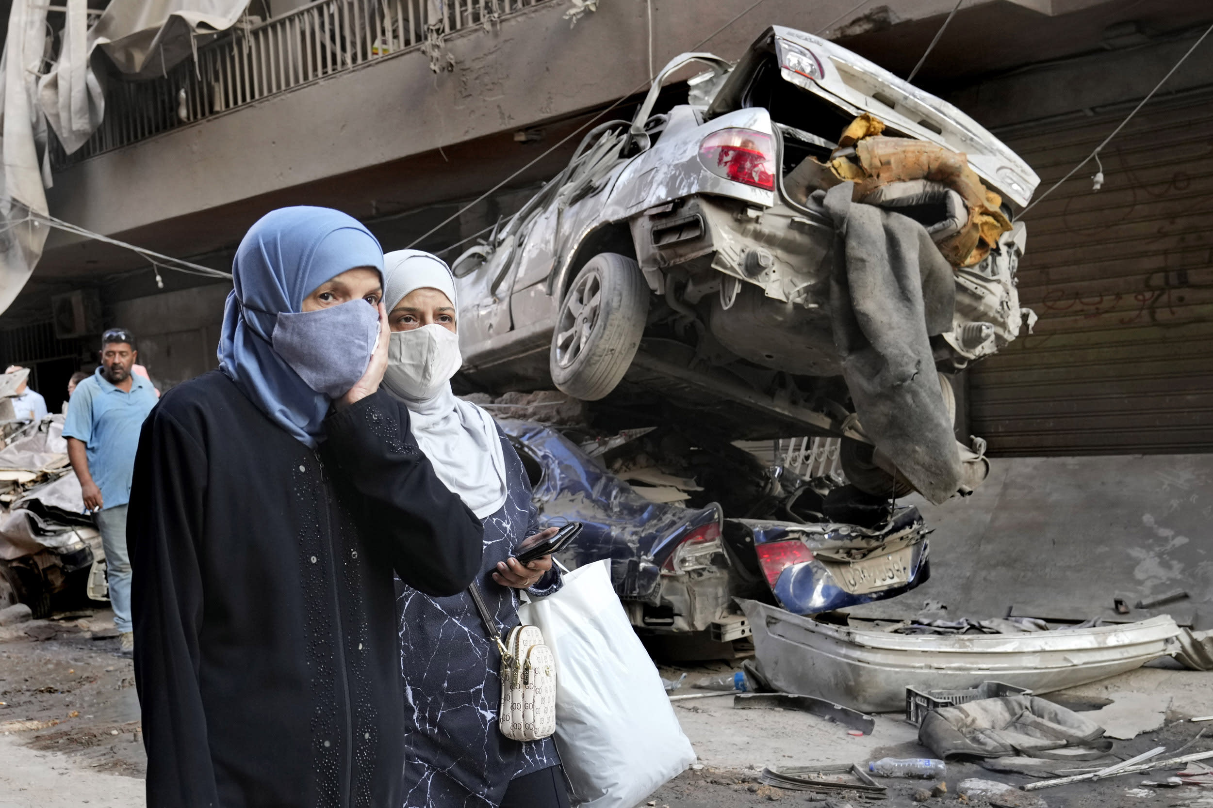 Lebanese women pass near destroyed cars at the site of an Israeli airstrike in Beirut.