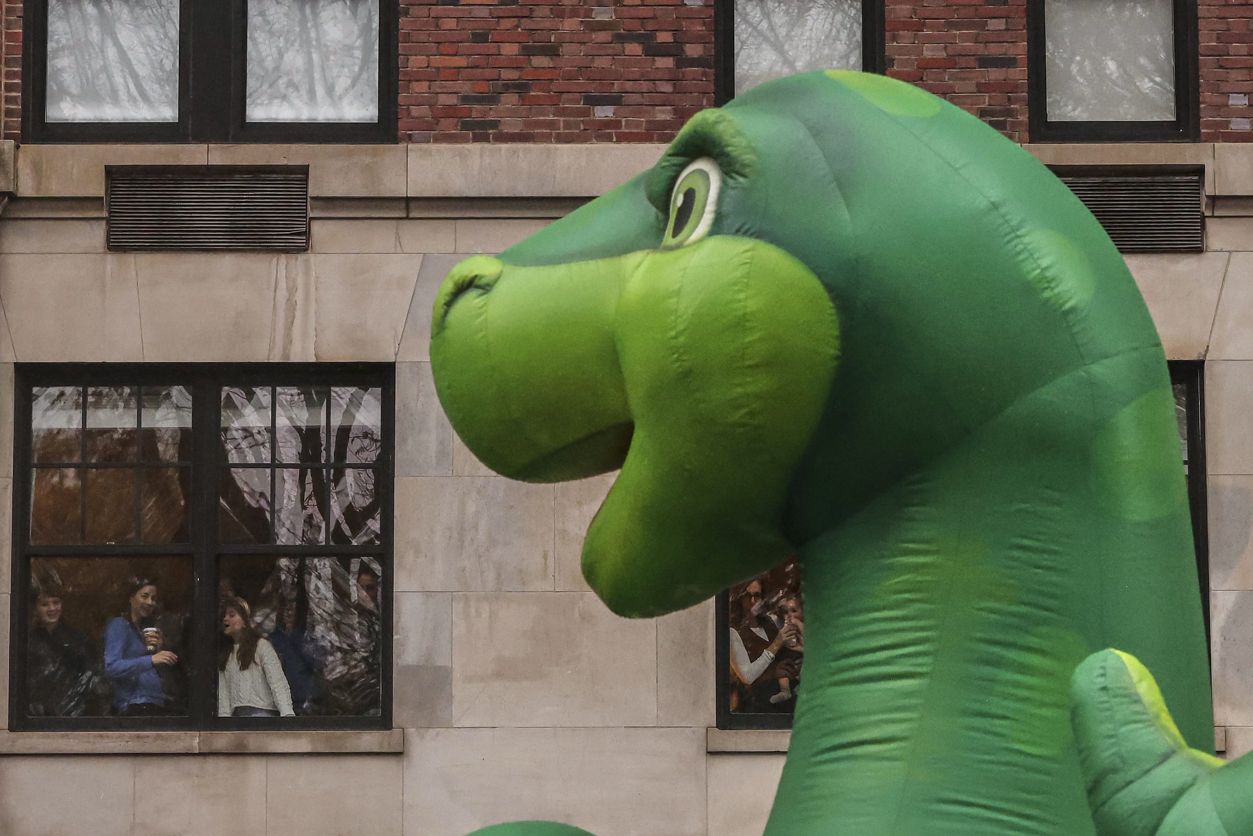 Spectators watch from an apartment window as the Sinclair's Dino balloon passes by.
