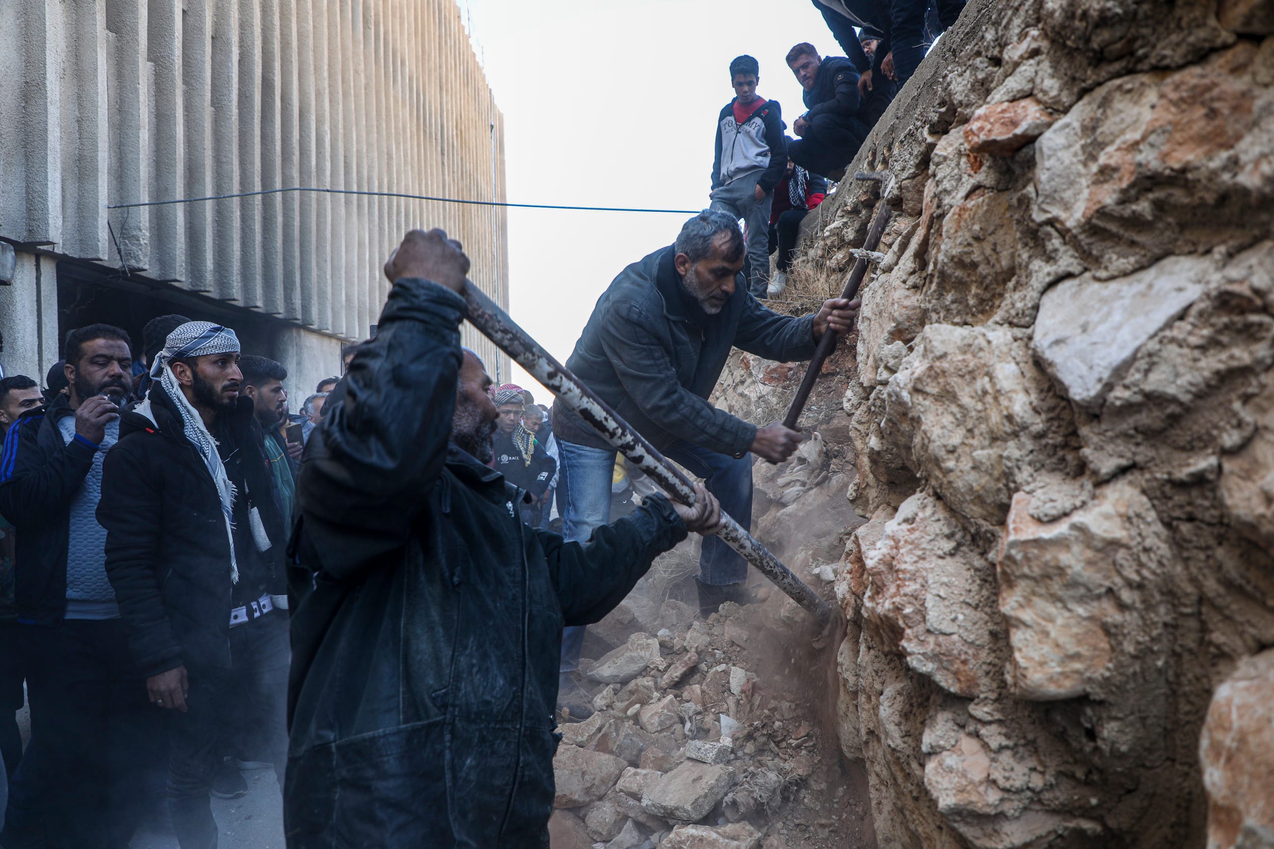 People chip away at a wall.