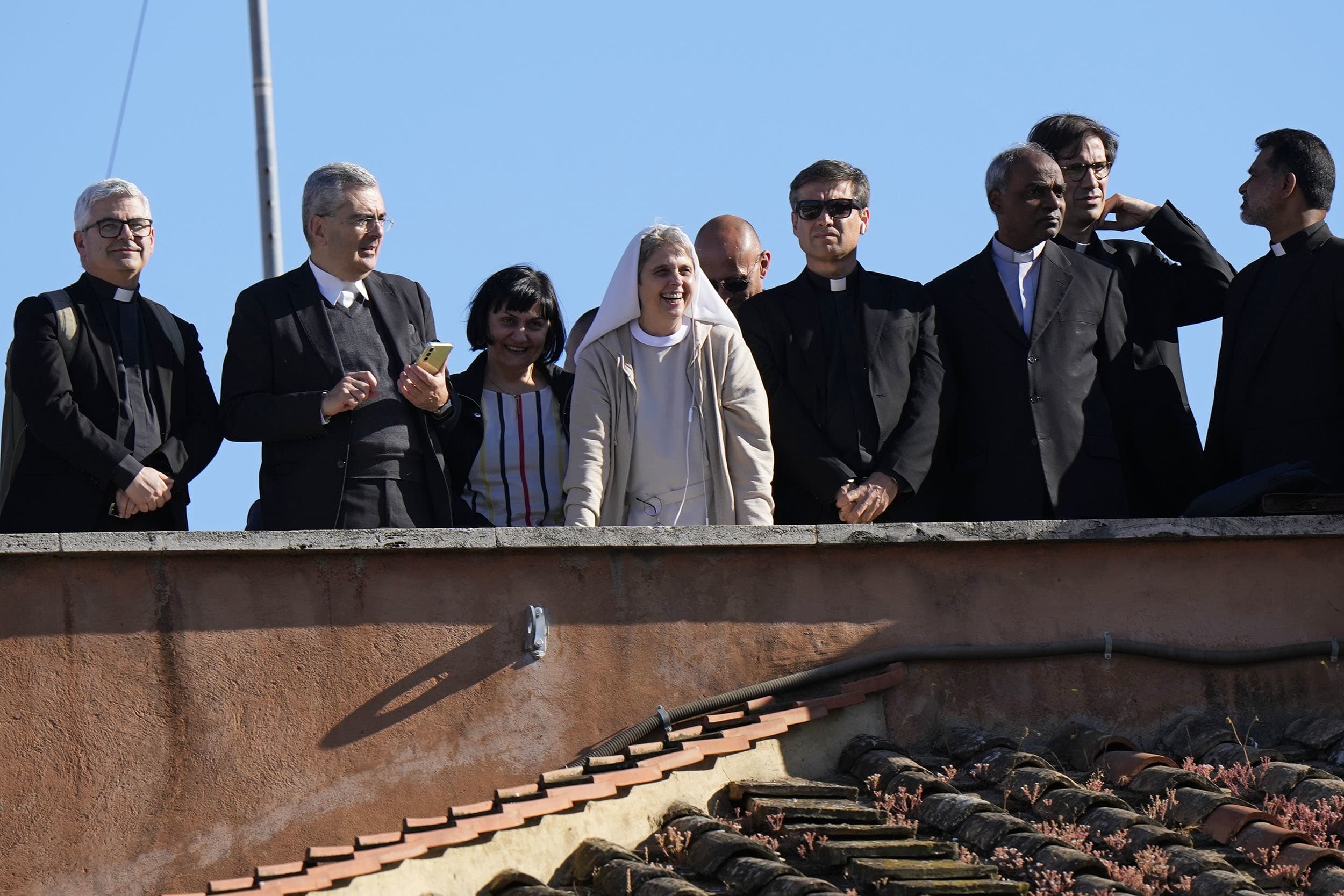 Clergy stand on a rooftop terrace as they wait to see the smoke billow from the chimney of the Sistine Chapel