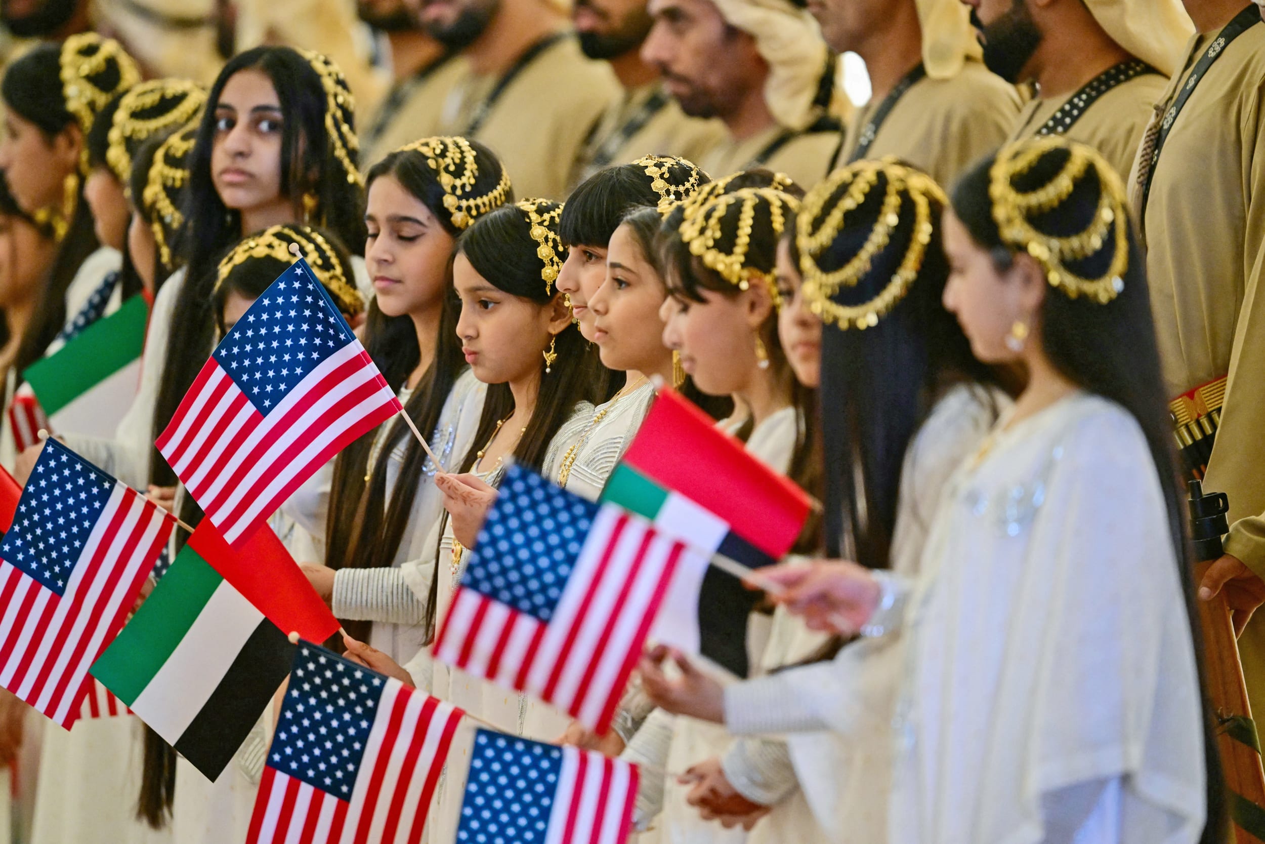 Girls dressed in traditional attire carry UAE and US flags ahead of a welcome ceremony for President Donald Trump at the presidential terminal in Abu Dhabi ahead of US President Donald Trump's arrival to the United Arab Emirates (UAE) on May 15, 2025. 