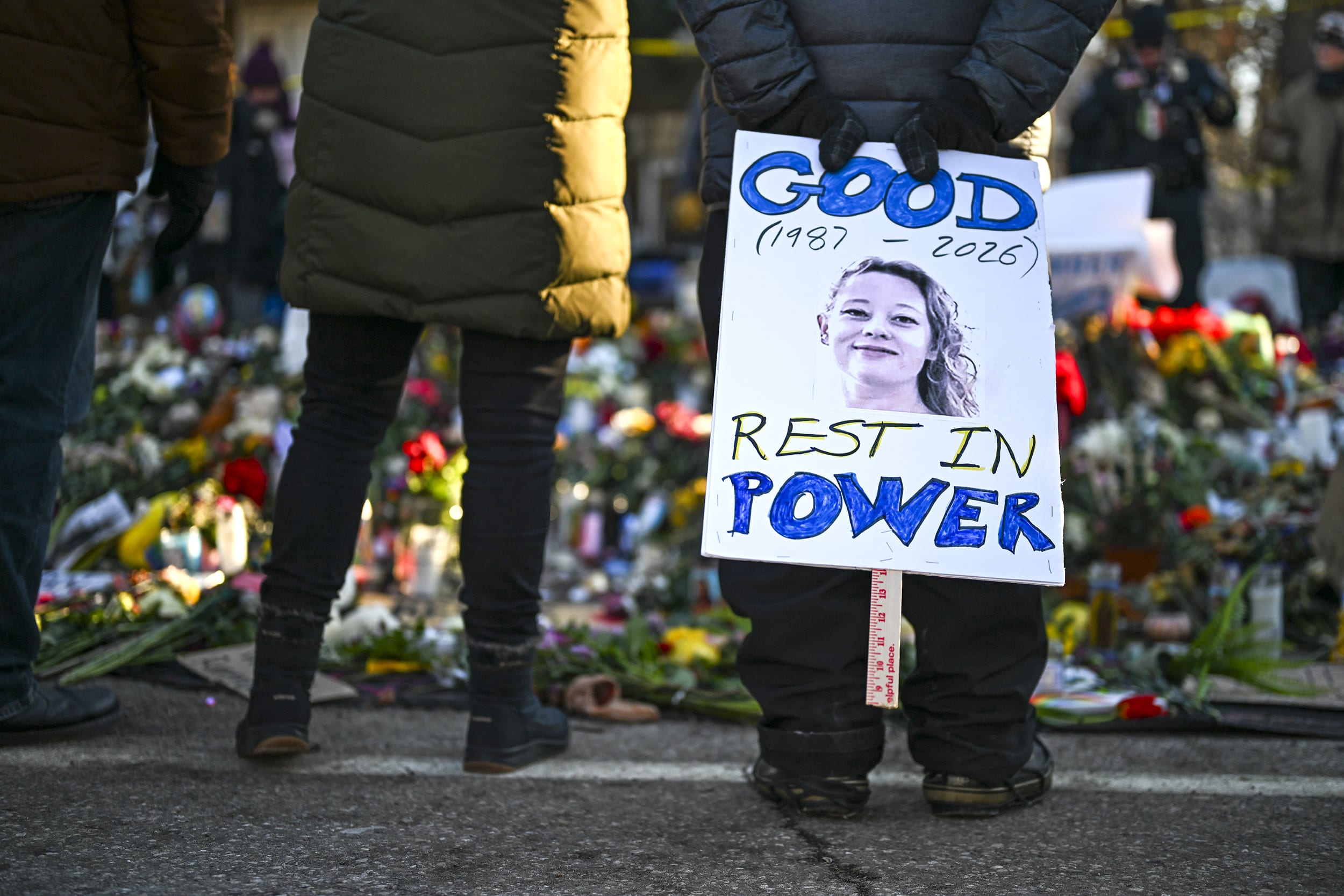 Image: A person holds a sign reading "Good Rest in Power" during a vigil at a memorial near the site where Renee Good was killed