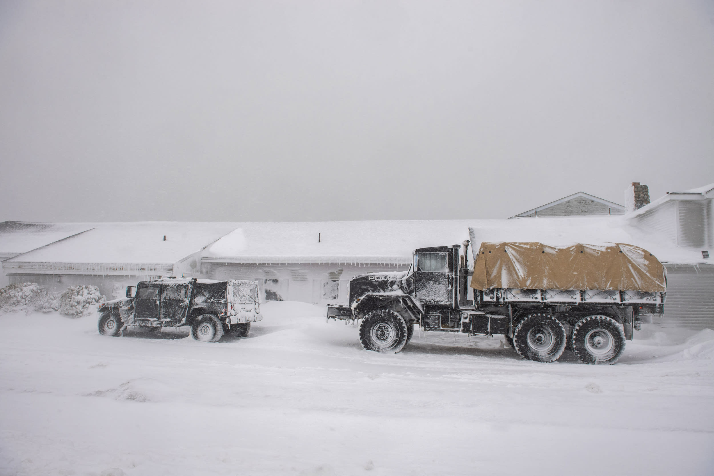 Two National Guard high-water vehicles stand ready in a blizzard storm in case of flooding.