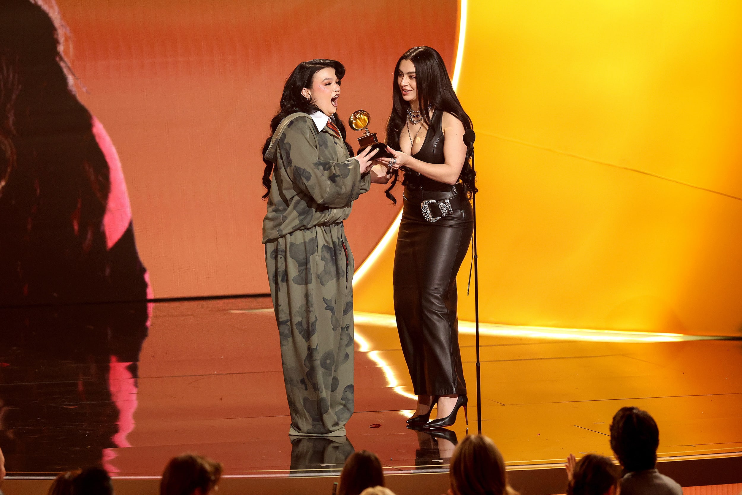 Charli XCX hands Lola Young a Grammy award onstage.