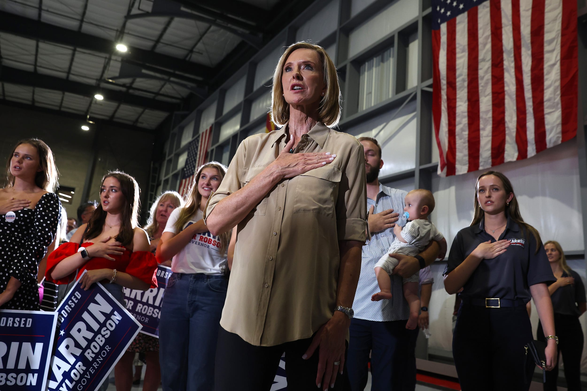 Karrin Taylor Robson Campaigns For Governor Of Arizona stands while pledging with a group of people in the background.