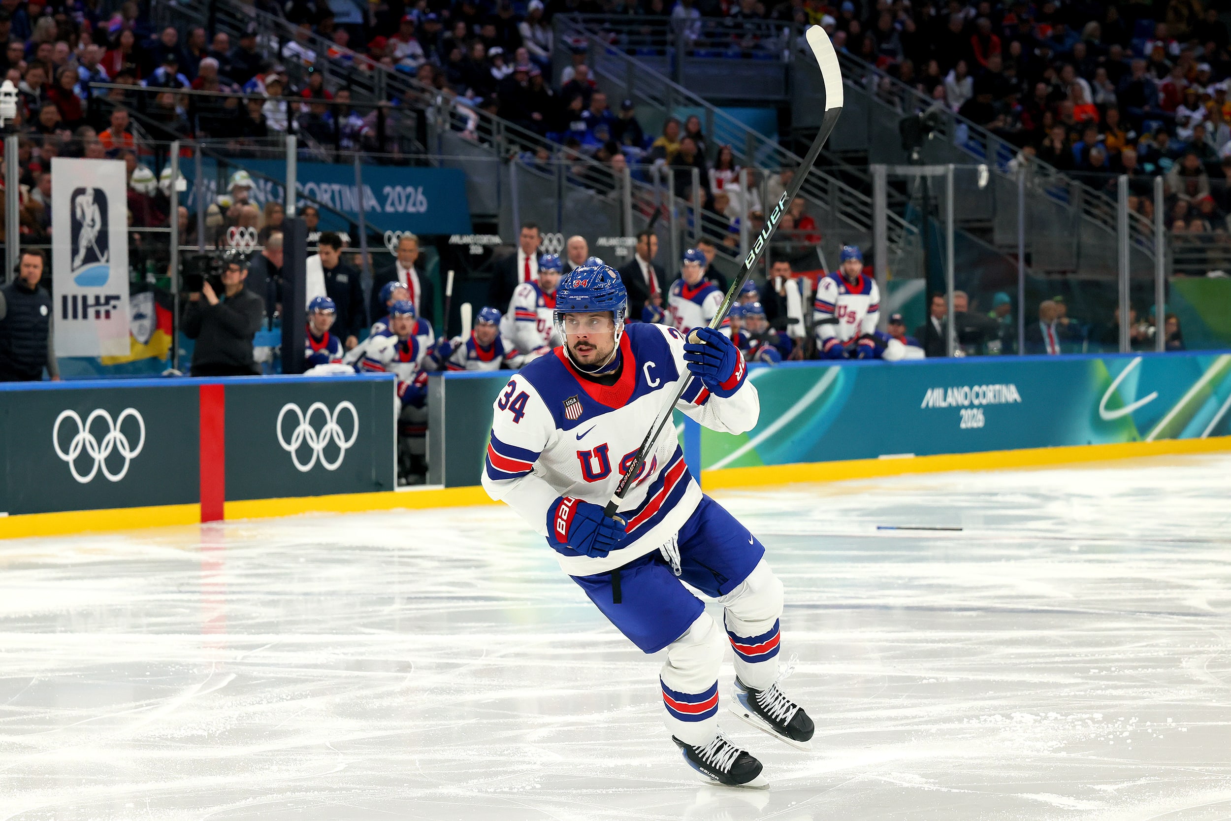 Auston Matthews turns on one ice skate while holding his hockey stick into the air with both hands.