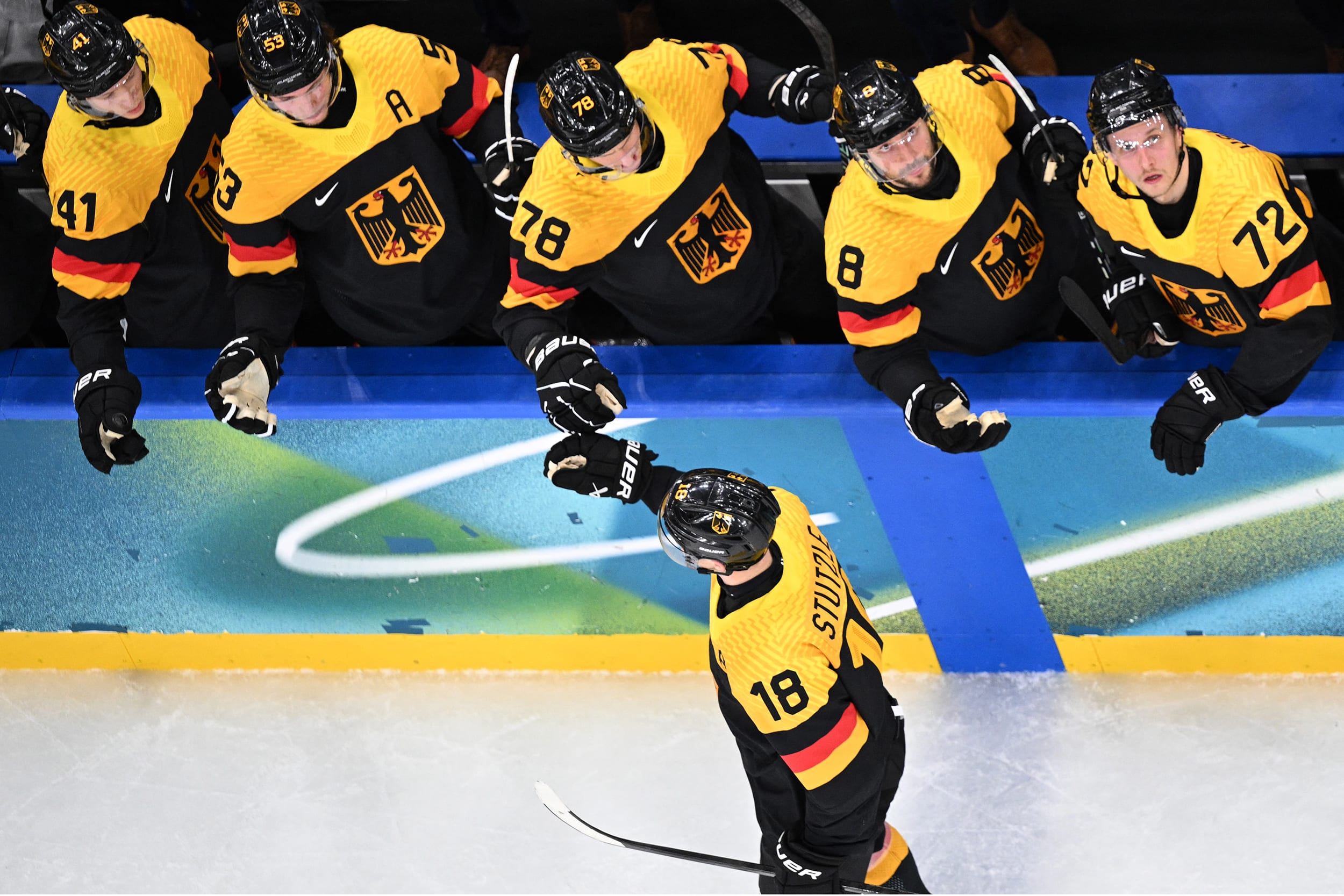 A hockey player high-fives his teammates as he skates past them on the ice.