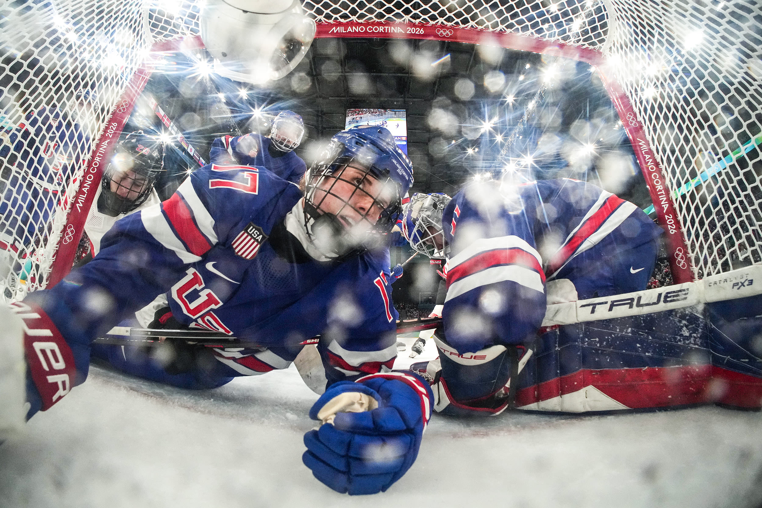 Two hockey players are seen lying on the ice from a remote camera positioned inside a goal.