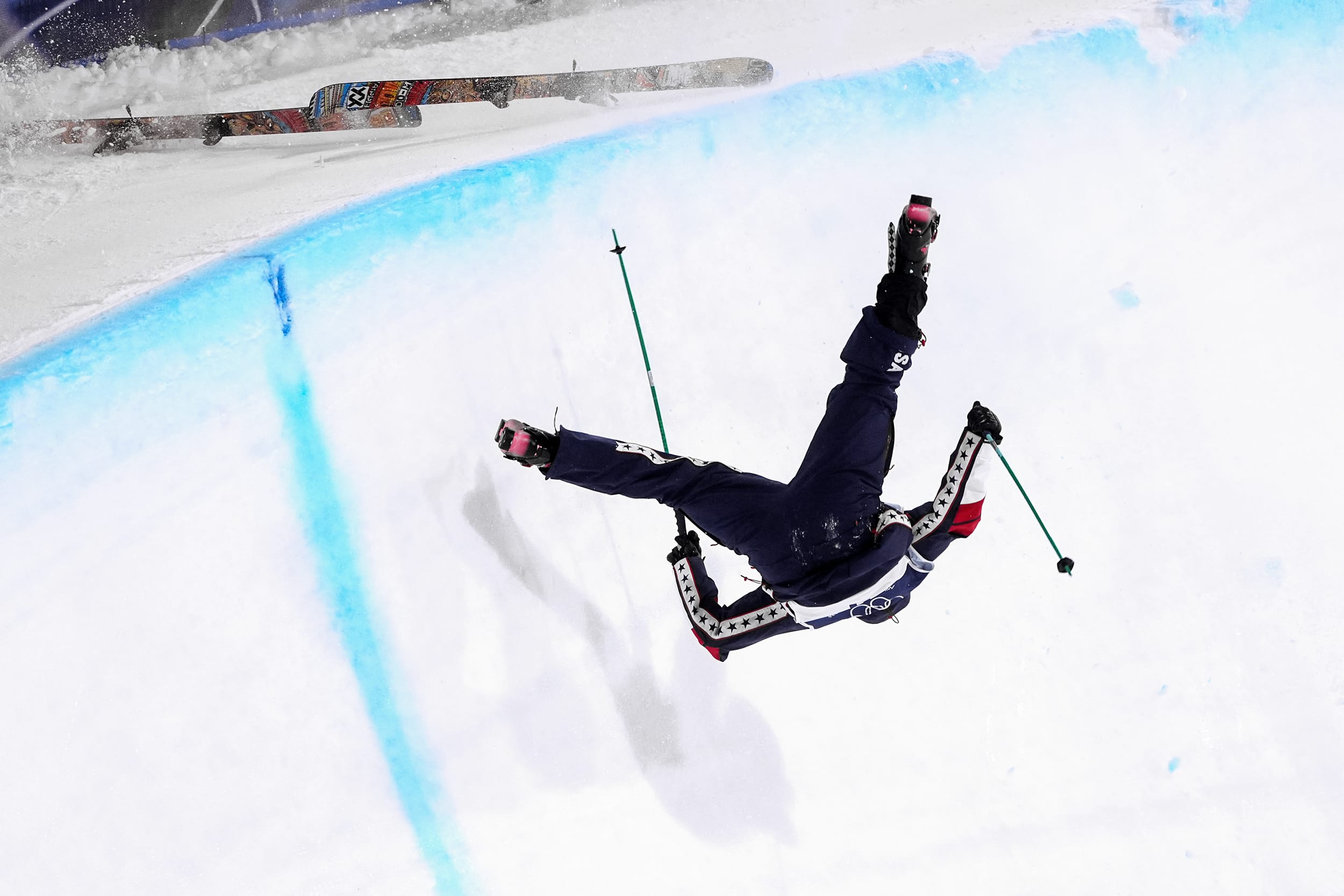 A skier falls head-first toward a sloped snowbank in a half-pipe.