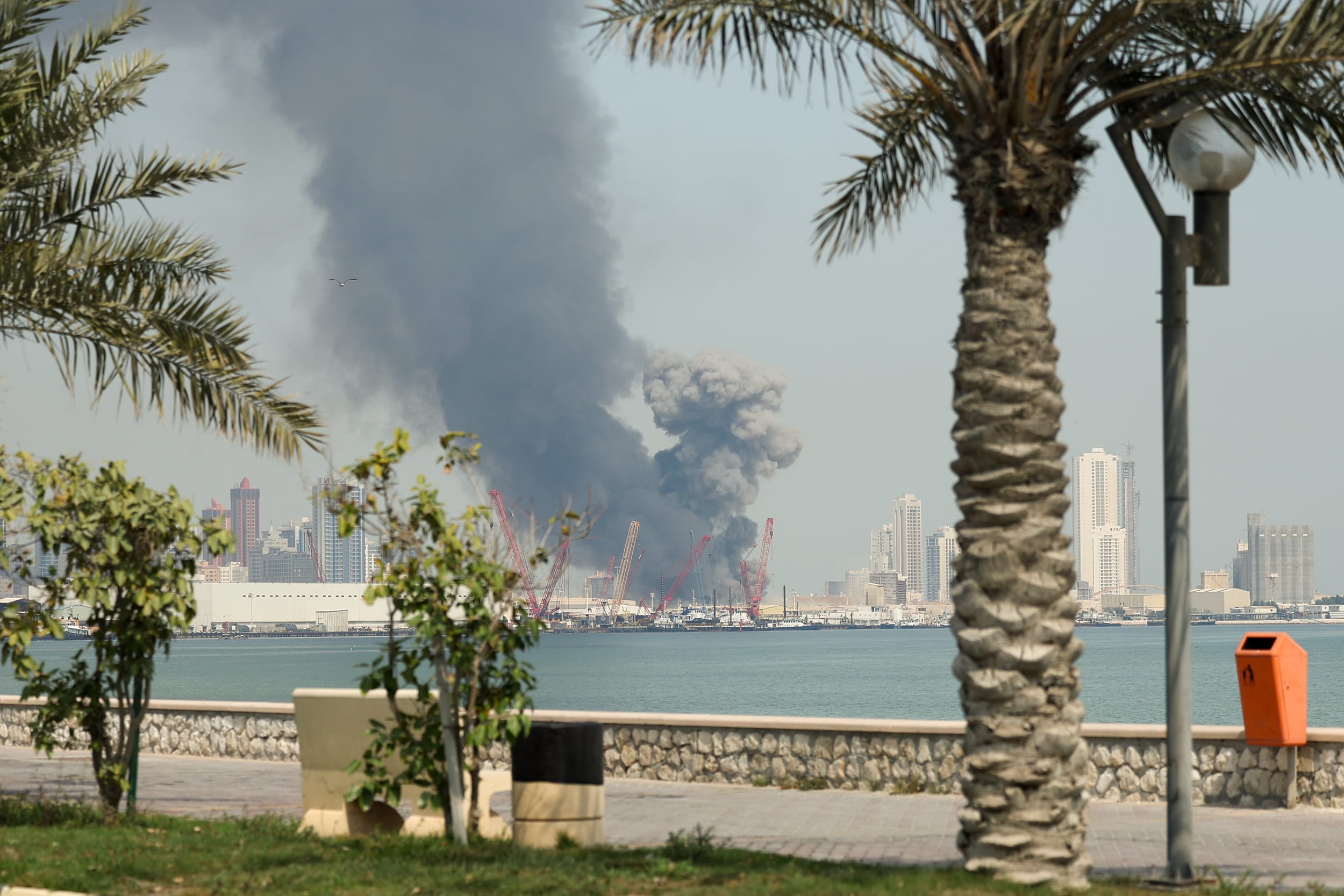 A tall black column of smoke rises from a port in the distance.