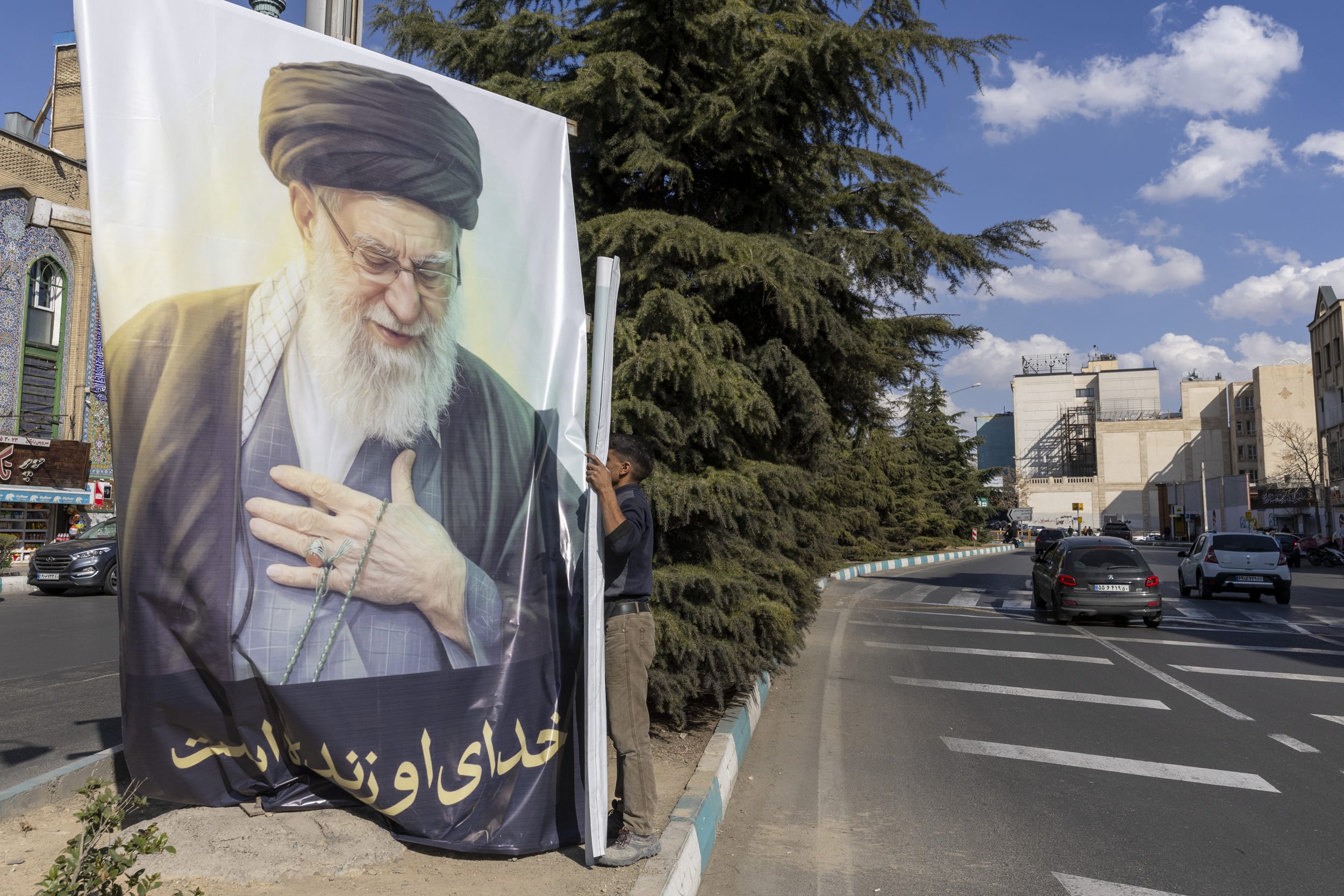 A man hangs a poster featuring the late Ayatollah Ali Khamenei on March 5, 2026 in Tehran. 