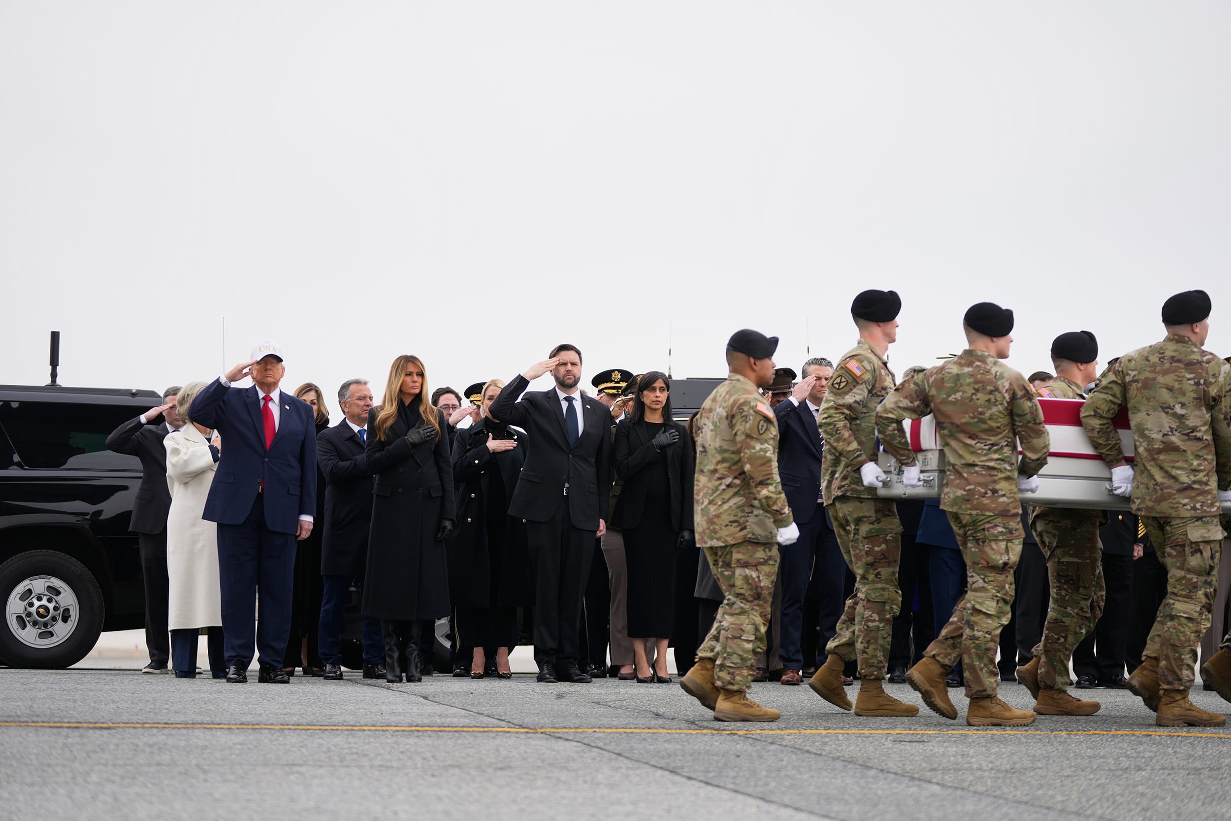 Donald Trump and JD Vance salute soldiers as they carry a coffin draped in an American flag across a tarmac.