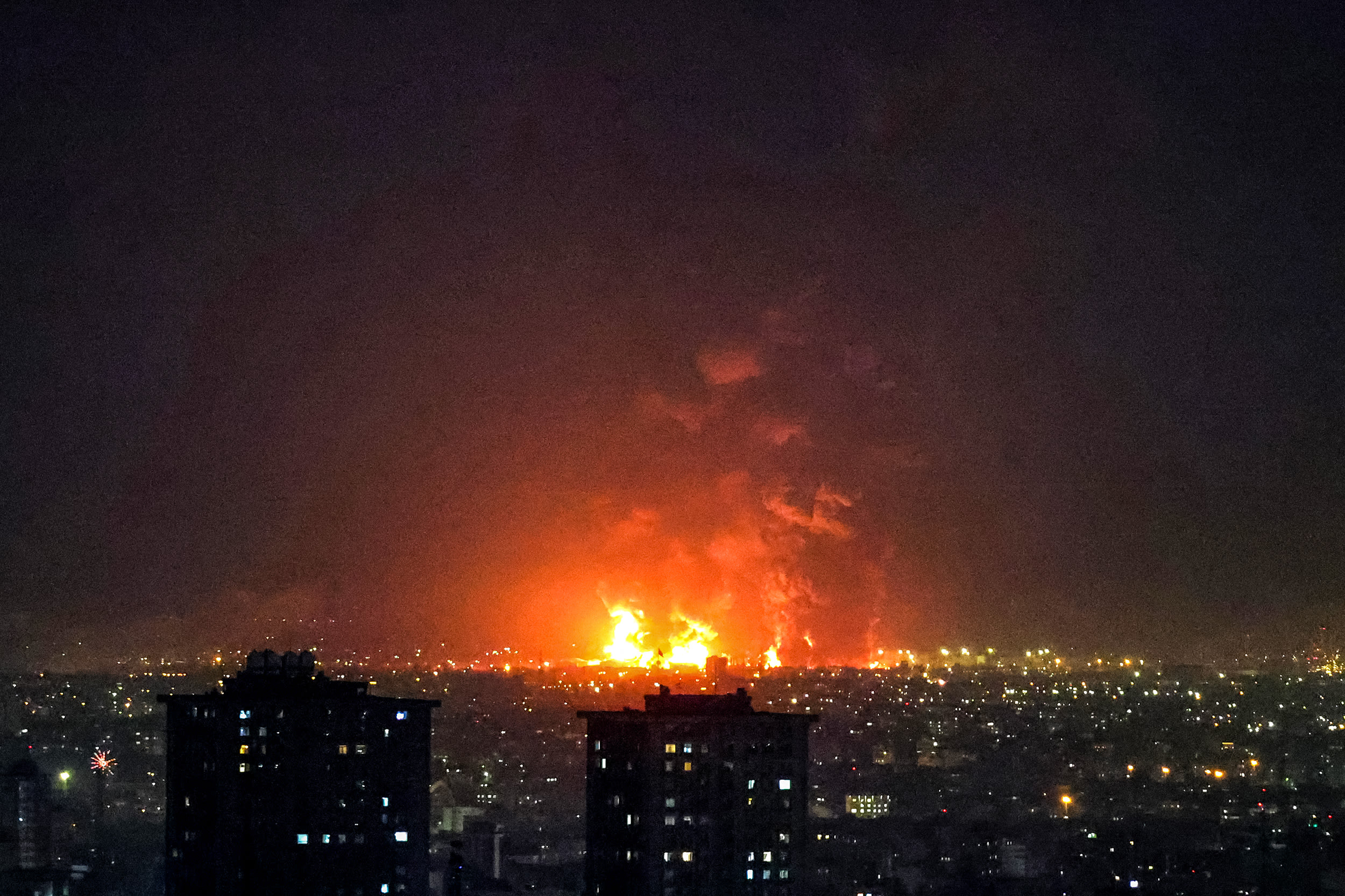 Flames can be seen rising into the sky from a distance over the rooftops of Tehran at night.