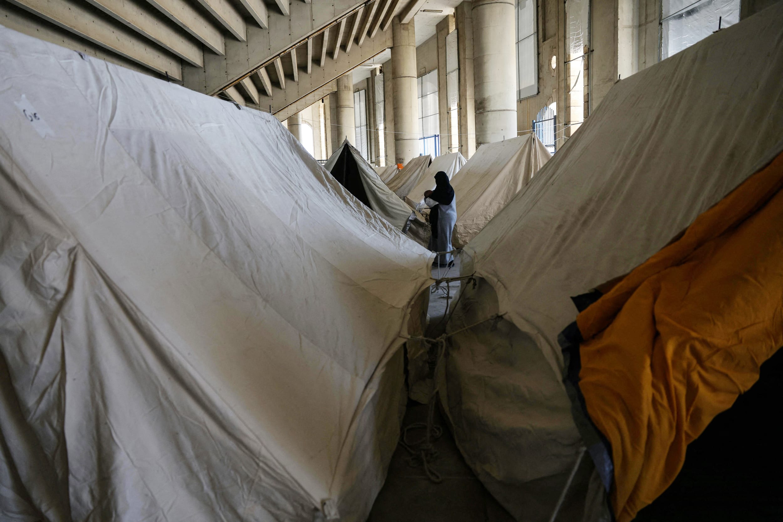 A displaced woman walks between tents inside the Camille Chamoun Sports City stadium