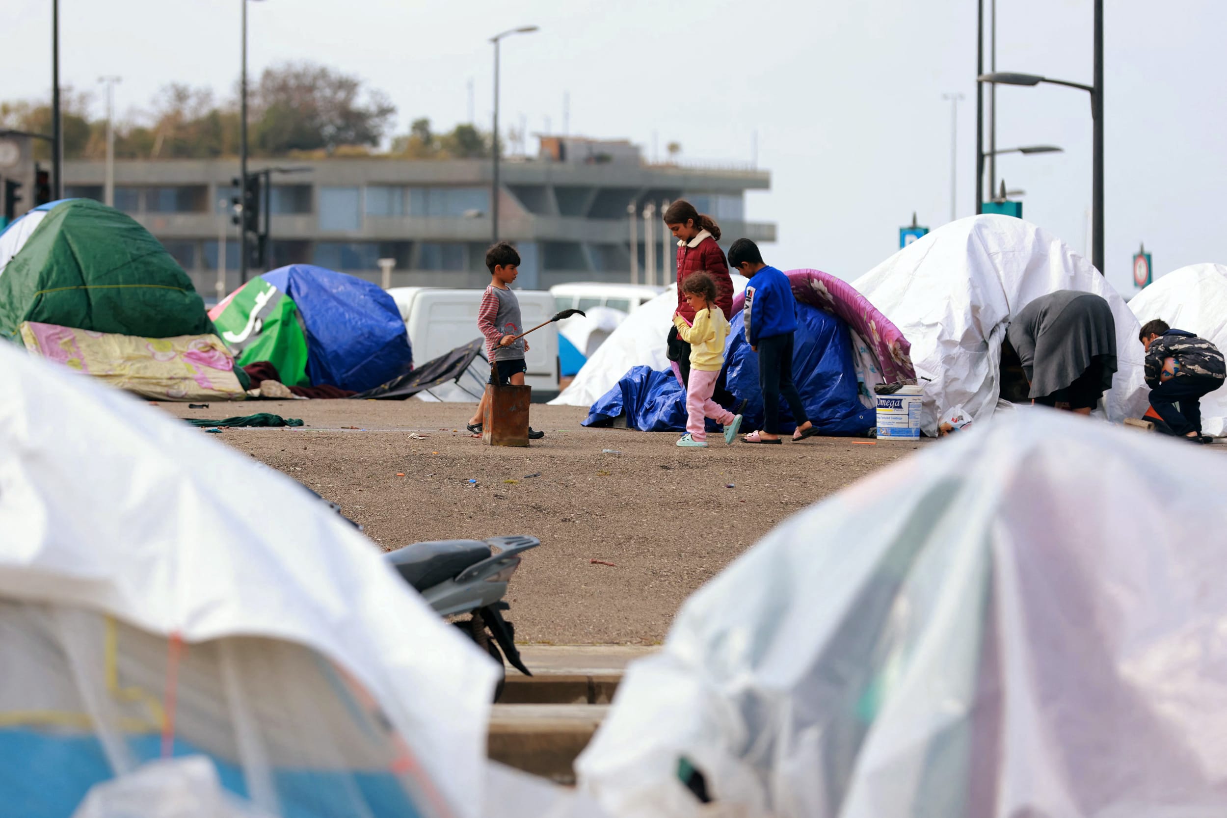 Displaced family members stand outside their tent covered in plastic sheeting to shield them from the stormy weather along Beirut's seafront area on March 15, 2026.