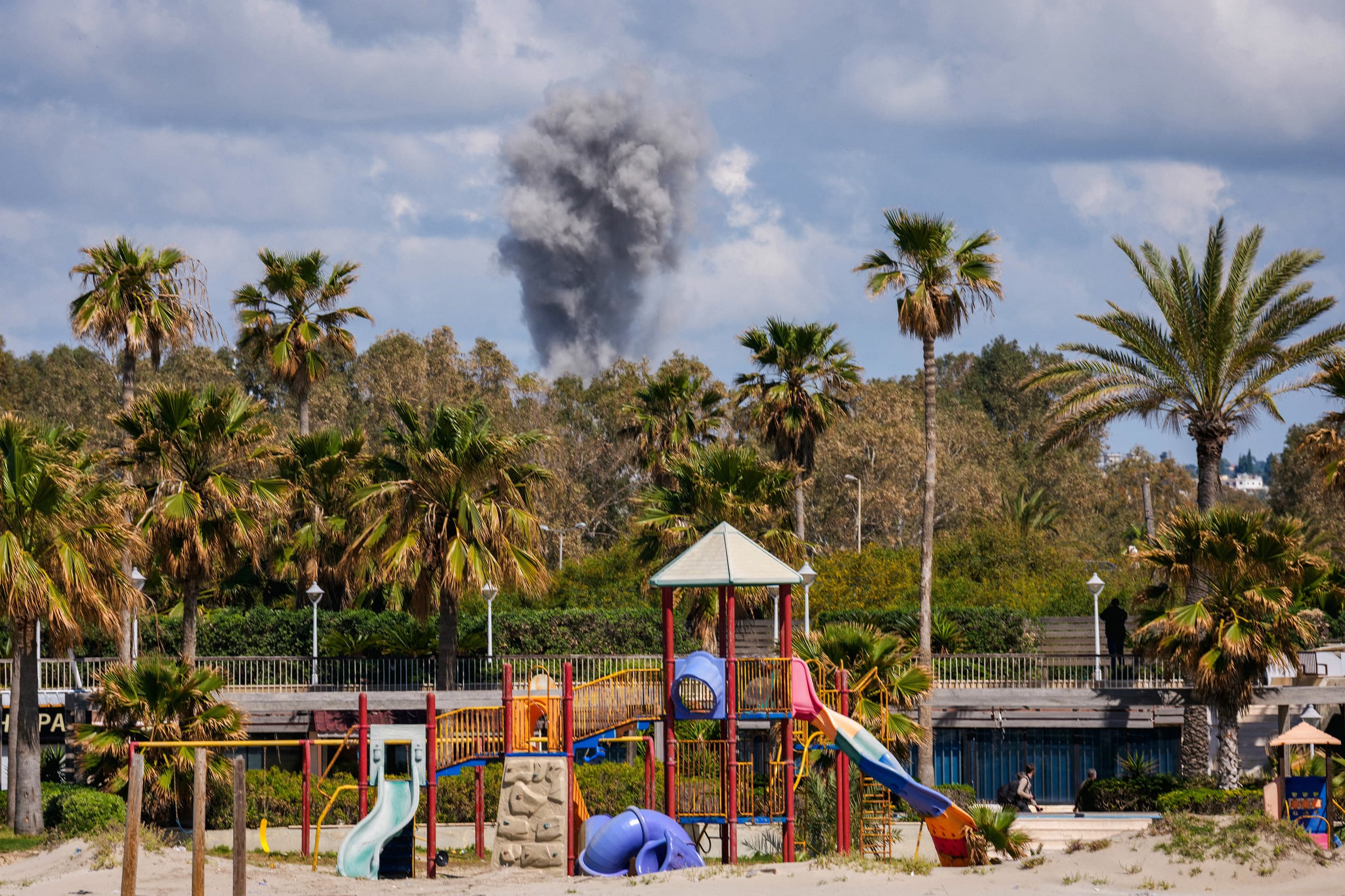 A playground stands empty as smoke rises in the distance from the site of an Israeli airstrike that targeted the outskirts of the southern city of Tyre, Lebanon, on March 24, 2026. 