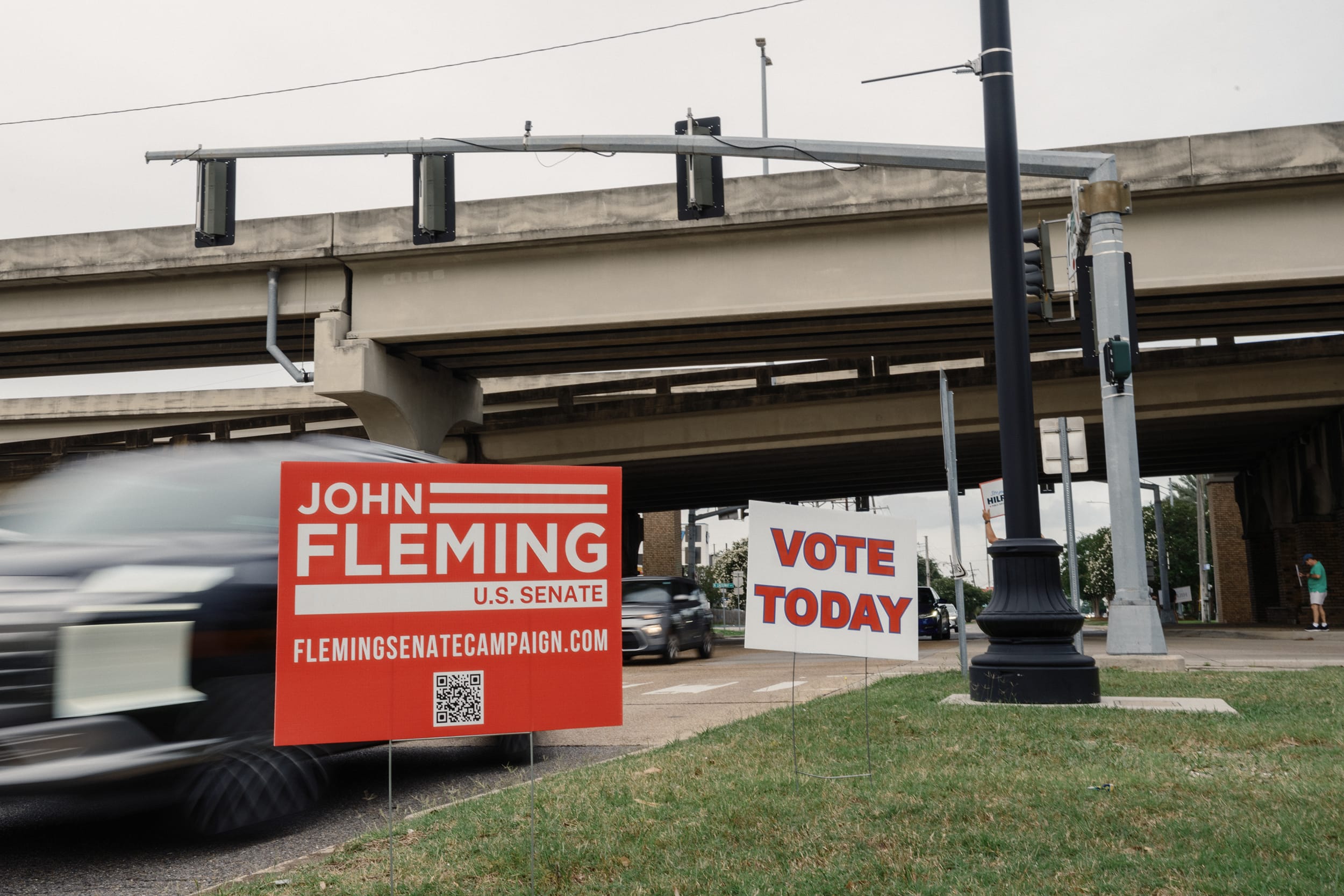 Red and white political signs at an intersection near a highway overpass.