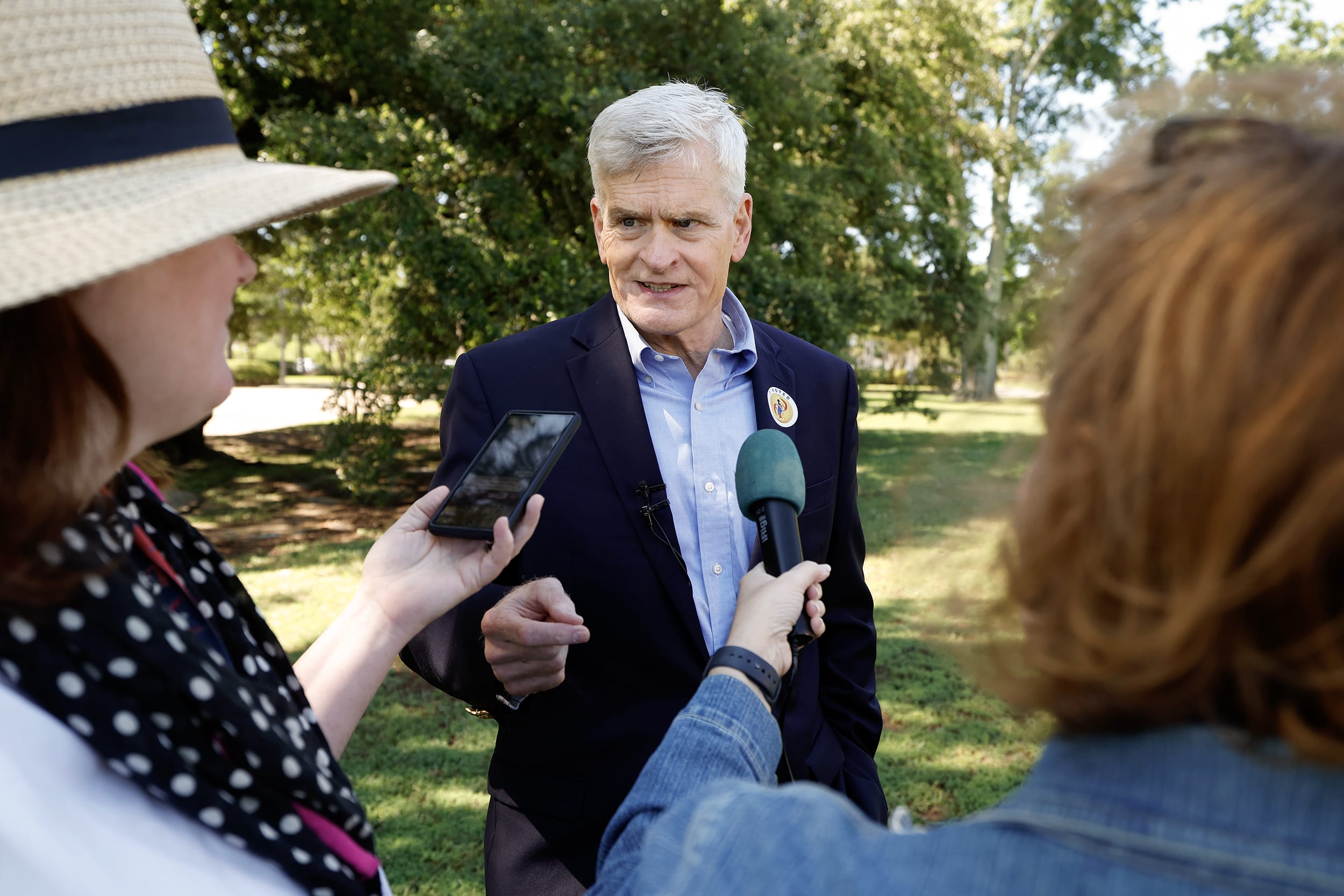 Bill Cassidy speaking to two women holding a phone and microphone.