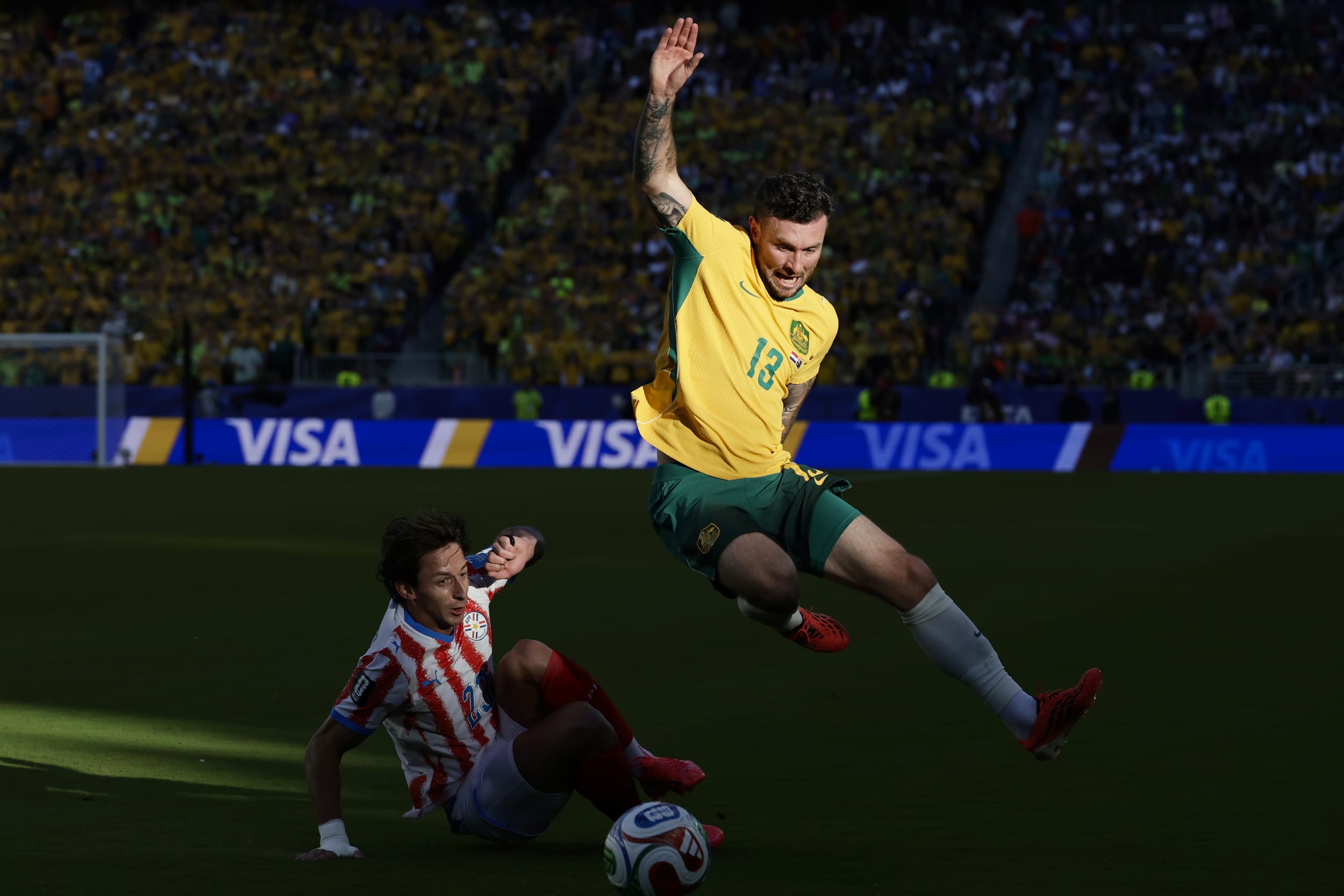Australia midfielder Aiden O'Neill (13) leaps over Paraguay midfielder Matías Galarza (23) during Paraguay vs Australia game.