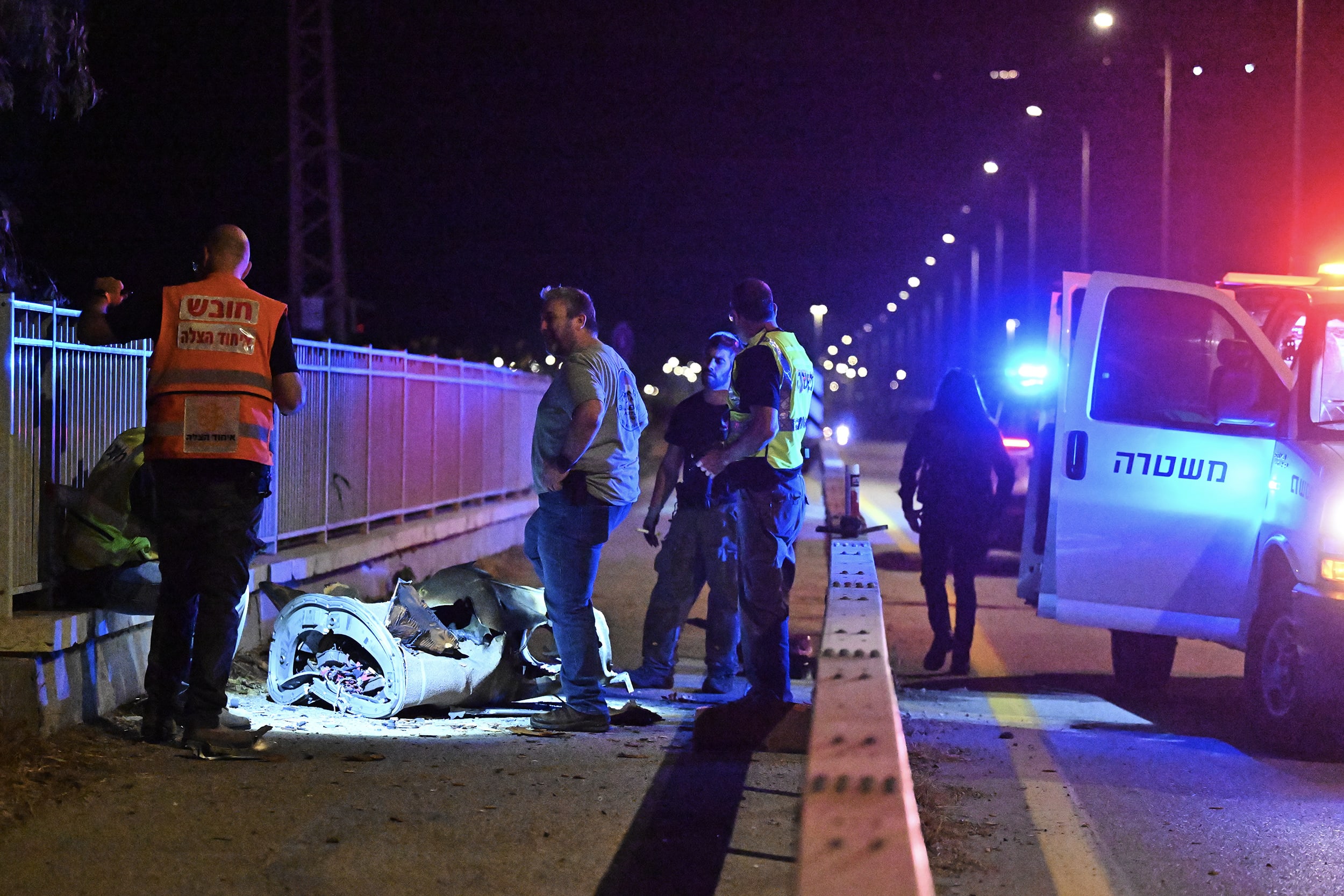 Emergency responders stand next to charred remnants of a rocket on a roadway.