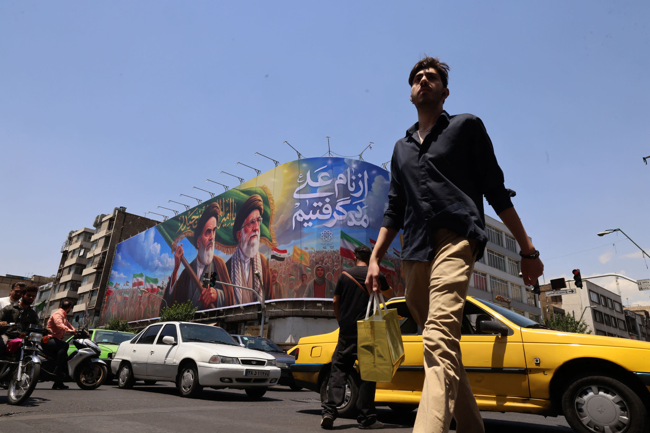 People cross the street past a large billboard showing portraits of Iran's late supreme leader, Ayatollah Ruhollah Khomeini, lefrt, ad slain supreme leader Ayatollah Ali Khamenei in central Tehran