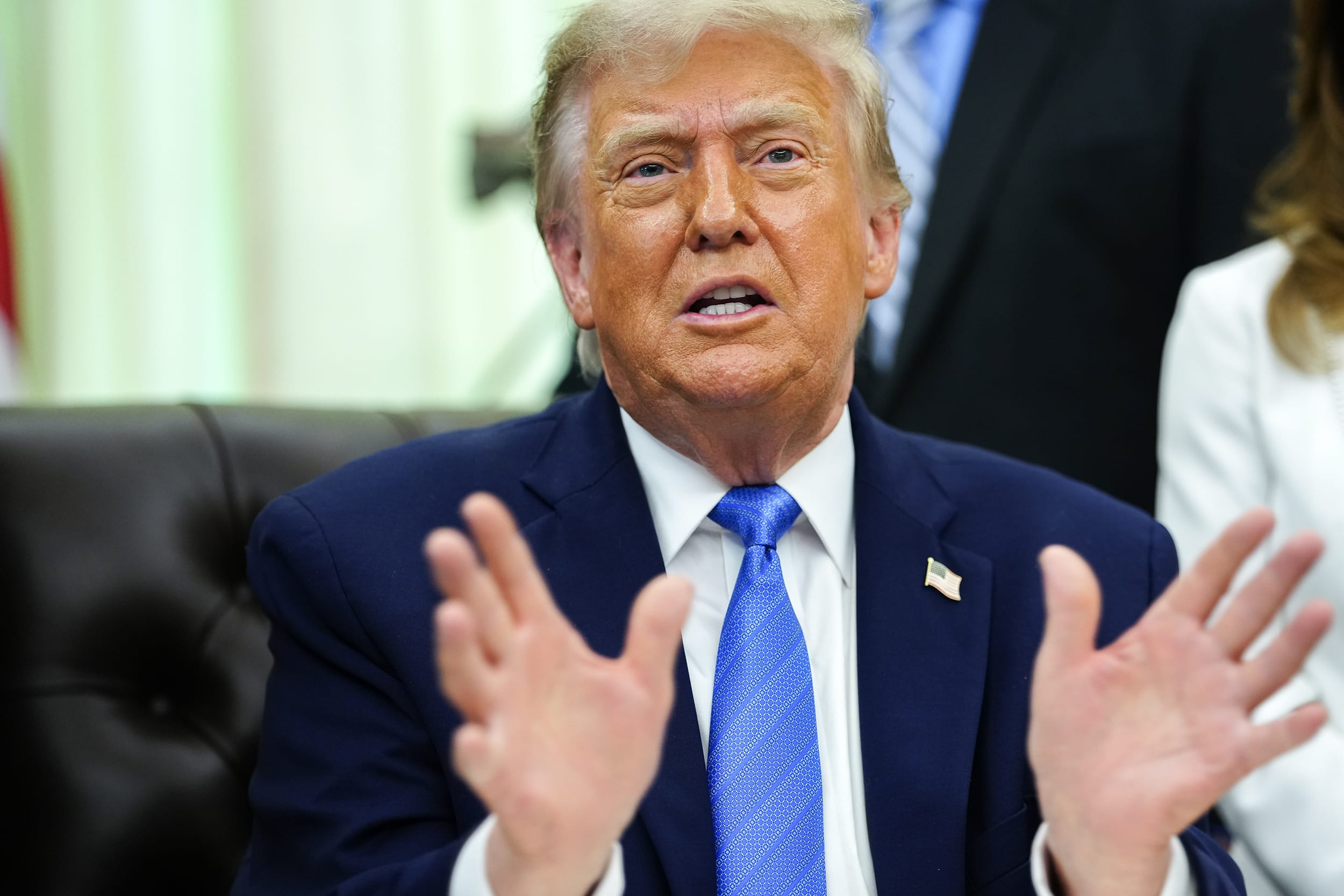 Donald Trump gesturing with both hands while seated in the Oval Office.