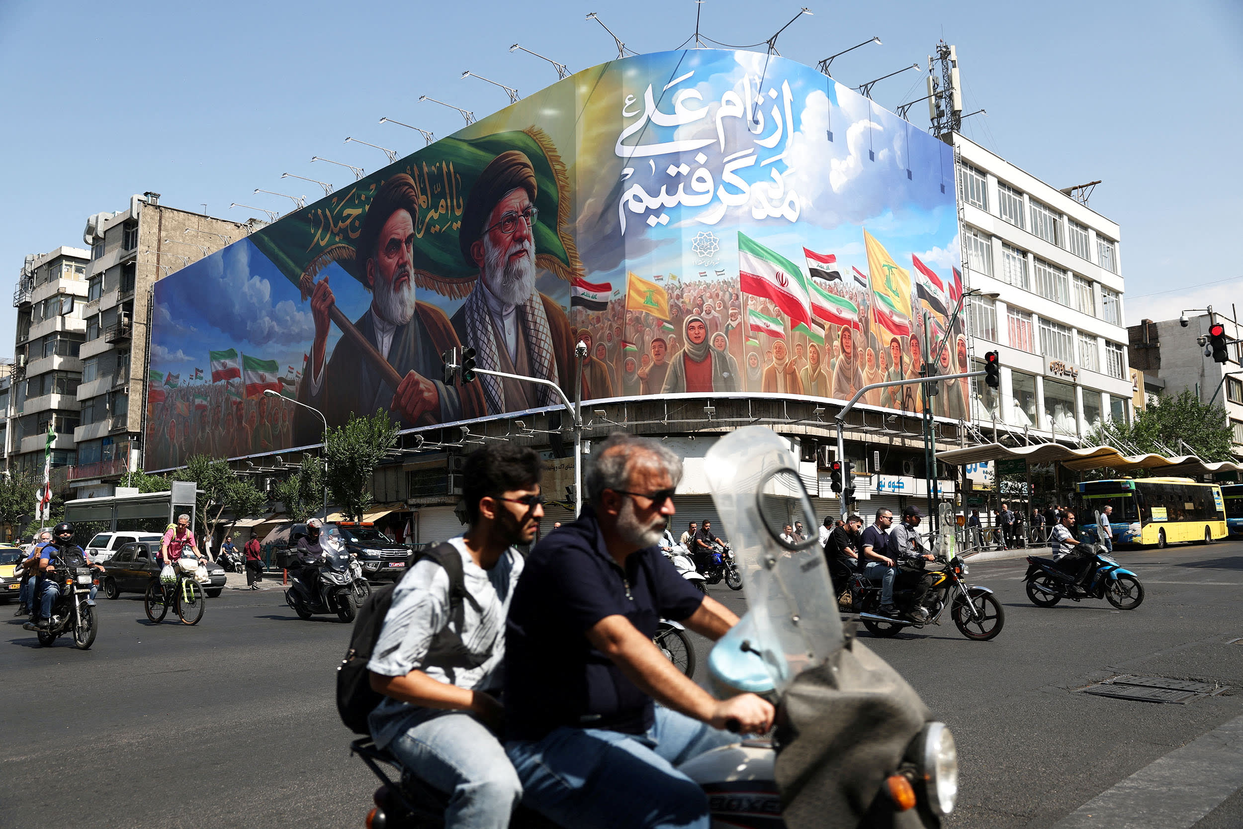 People ride past a billboard depicting the late leader of the Islamic Revolution, Ayatollah Ruhollah Khomeini, and the late Iran's Supreme Leader Ayatollah Ali Khamenei, on a street in Tehran