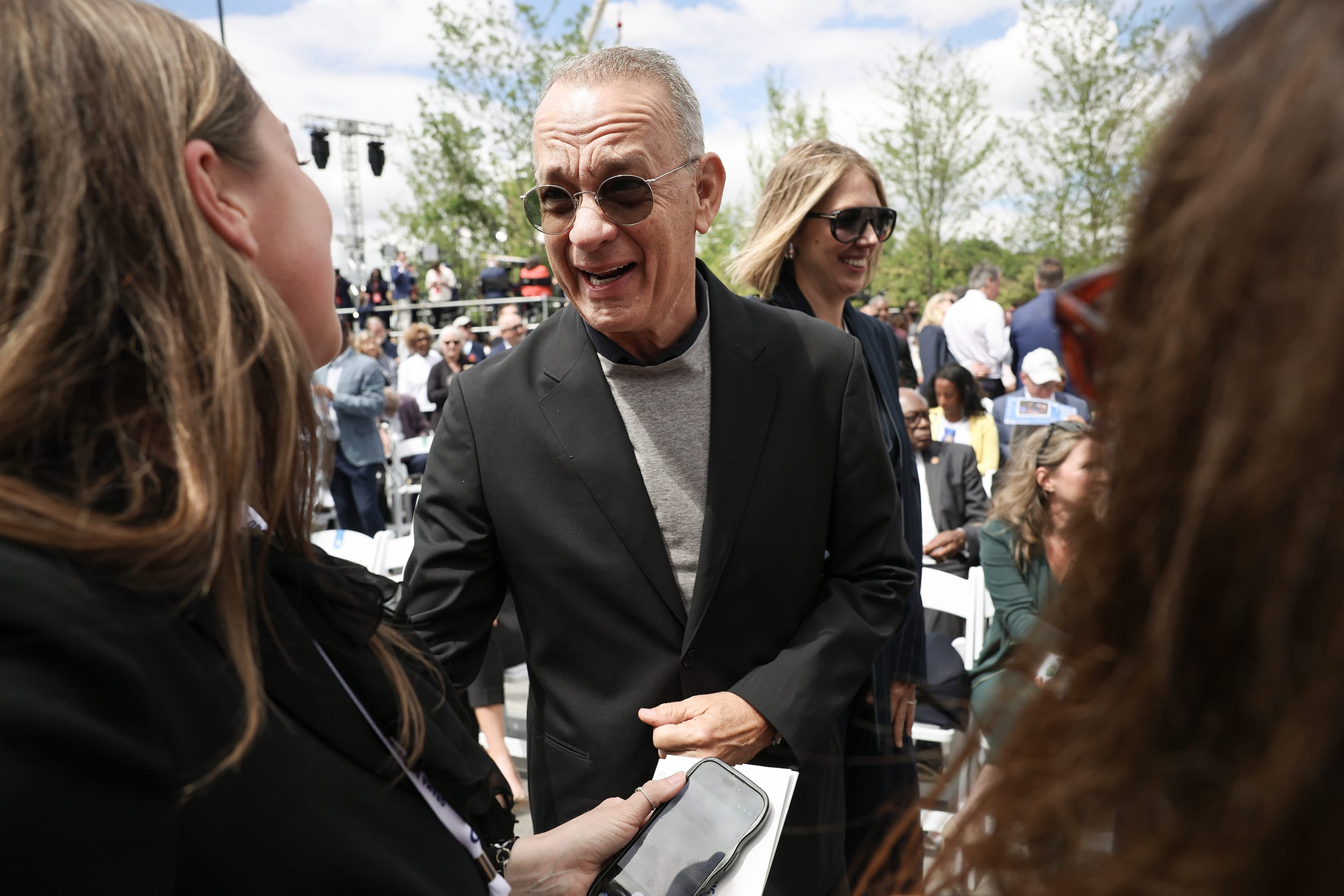 Tom Hanks at a crowded outdoor event wearing sunglasses.