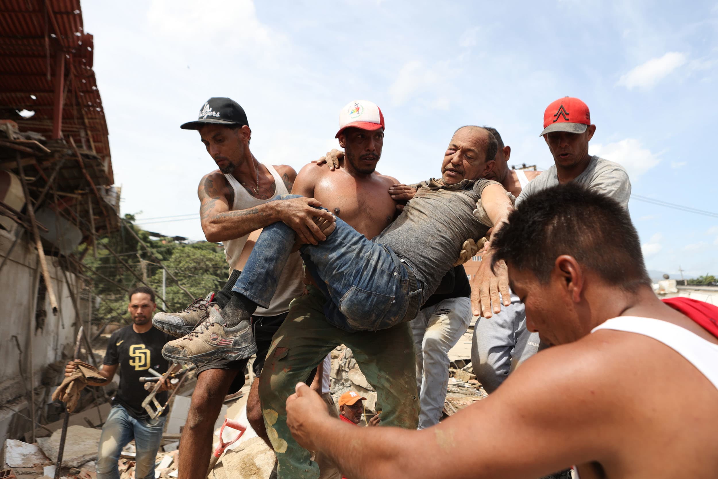 Neighbors carry a man rescued from the rubble of a collapsed building the day after earthquakes struck La Guaira, Venezuela, Thursday, June 25, 2026. 