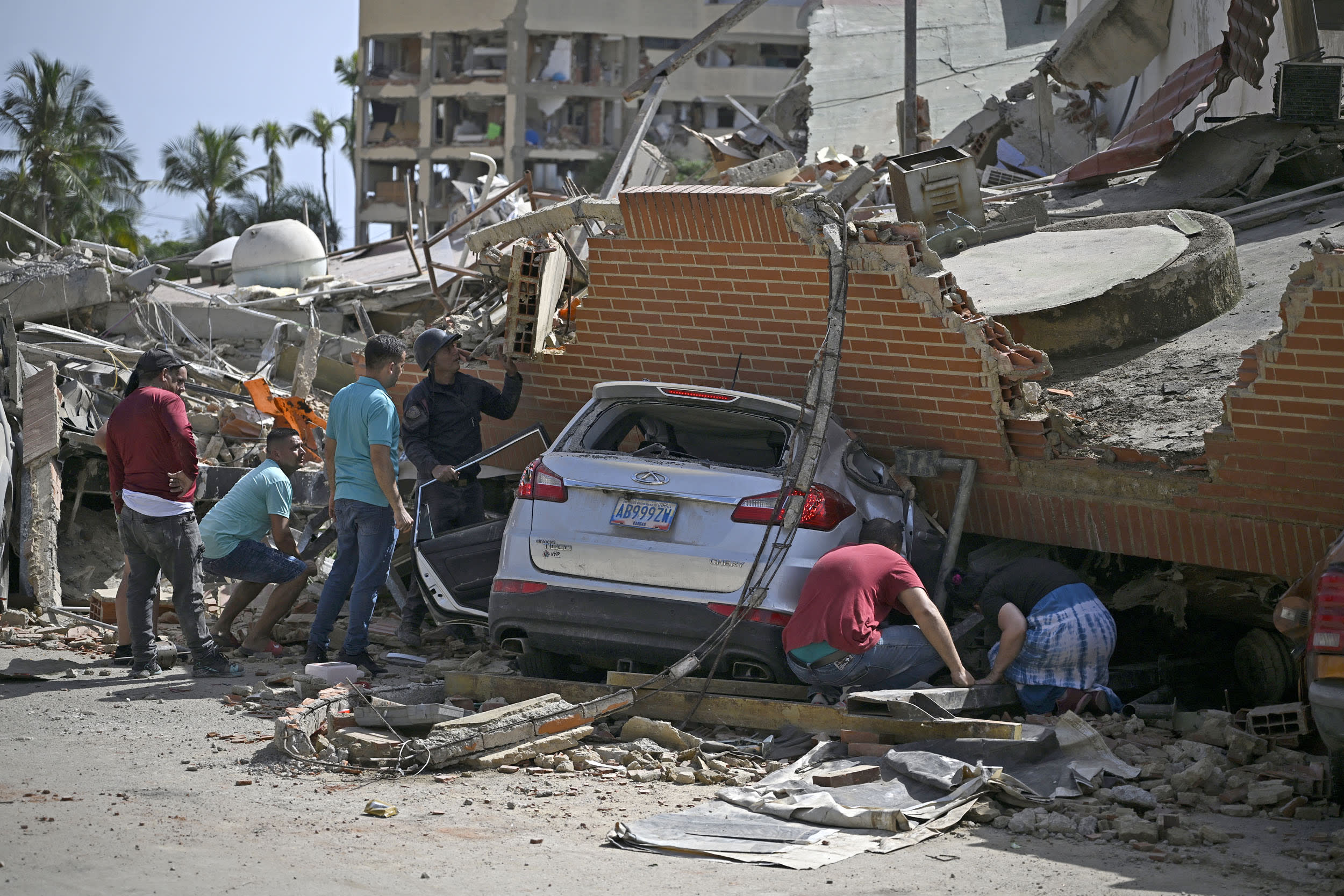 People search through the rubble around a car trapped beneath the collapsed remains of a residential building following an earthquake in Venezuela