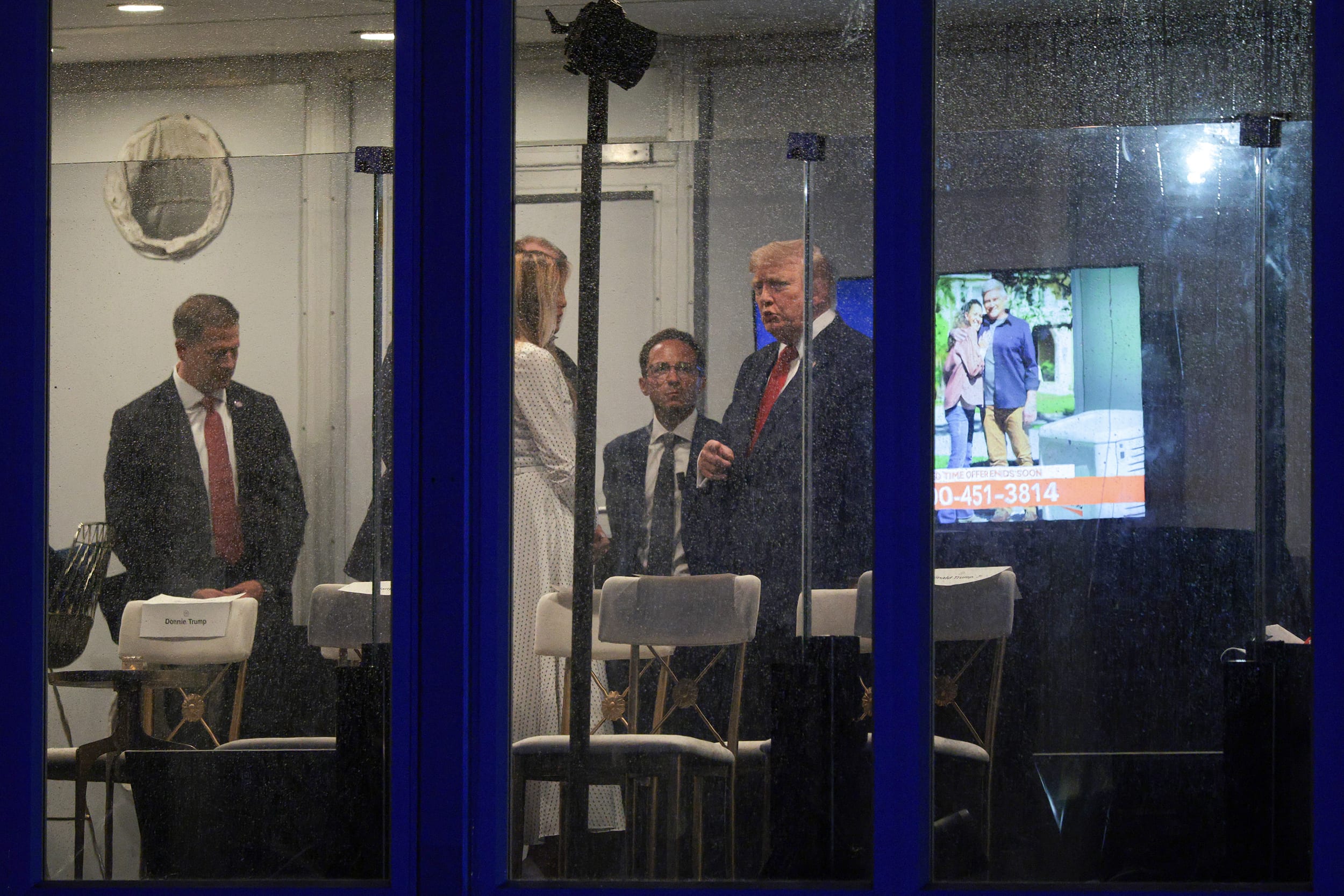 Donald Trump standing behind panels of wet glass.