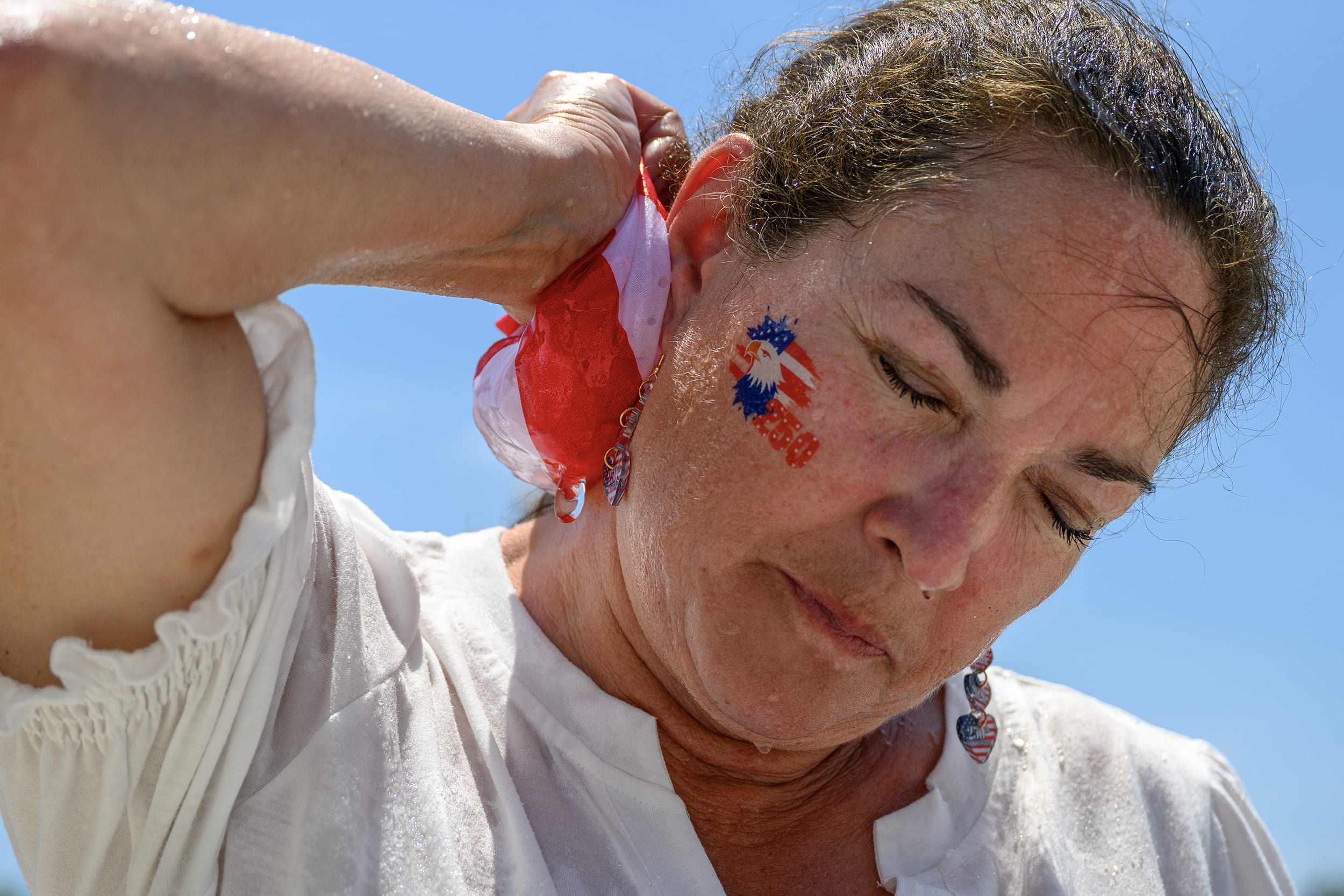 A woman with her eyes closed and a wet red and white cloth on her neck.