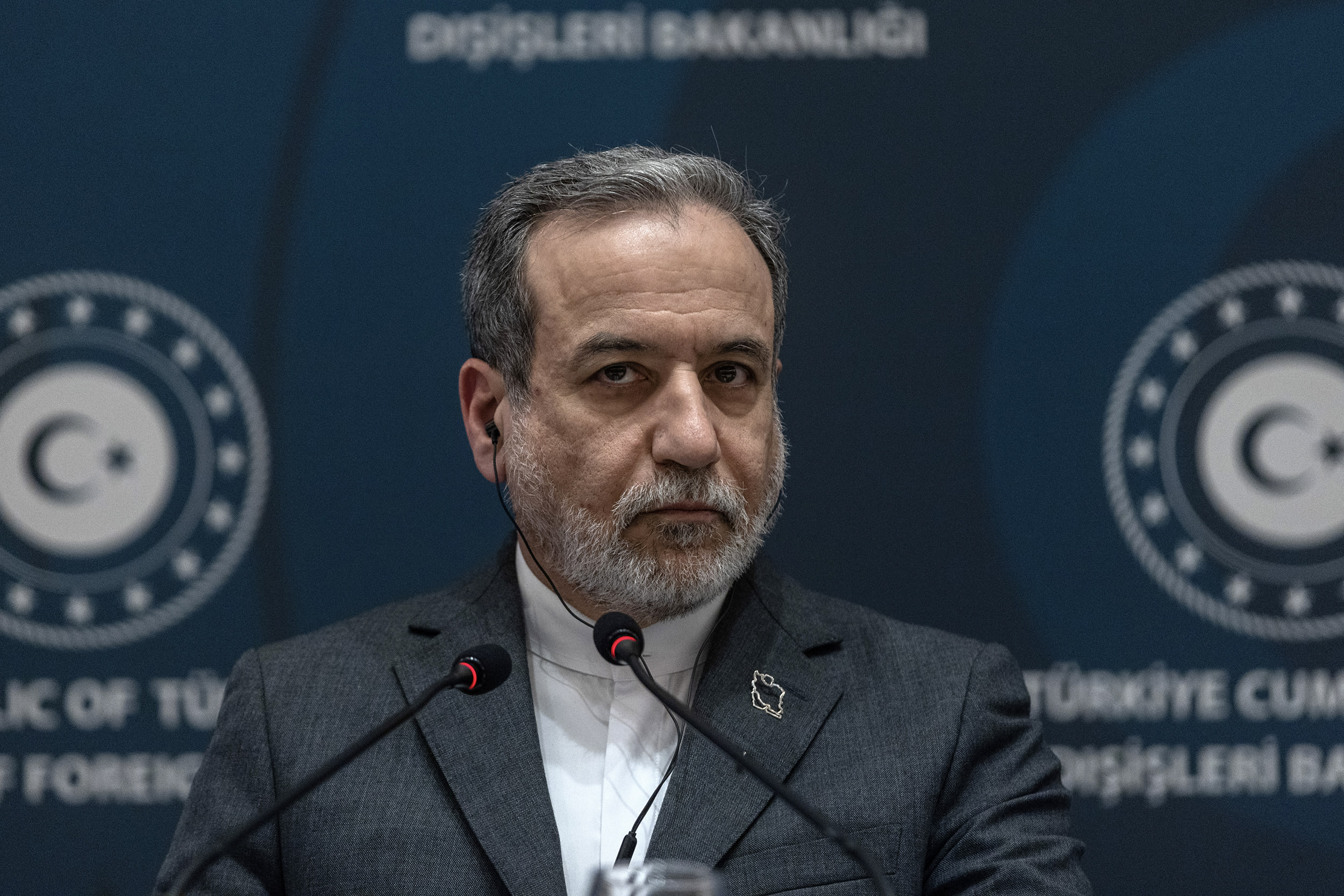 Abbas Araghchi looks toward the camera while seated in front of two microphones