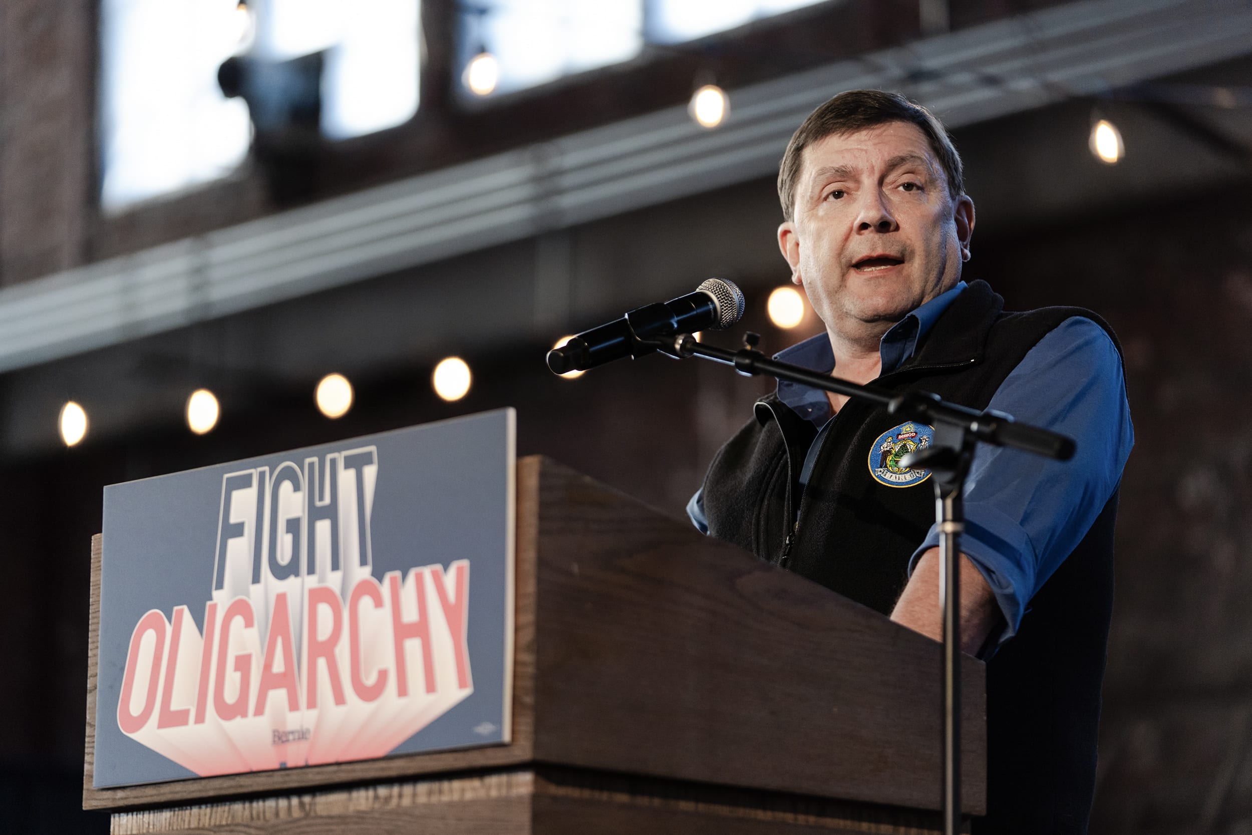 Troy Jackson speaking at a lectern with a sign reading FIGHT OLIGARCHY.