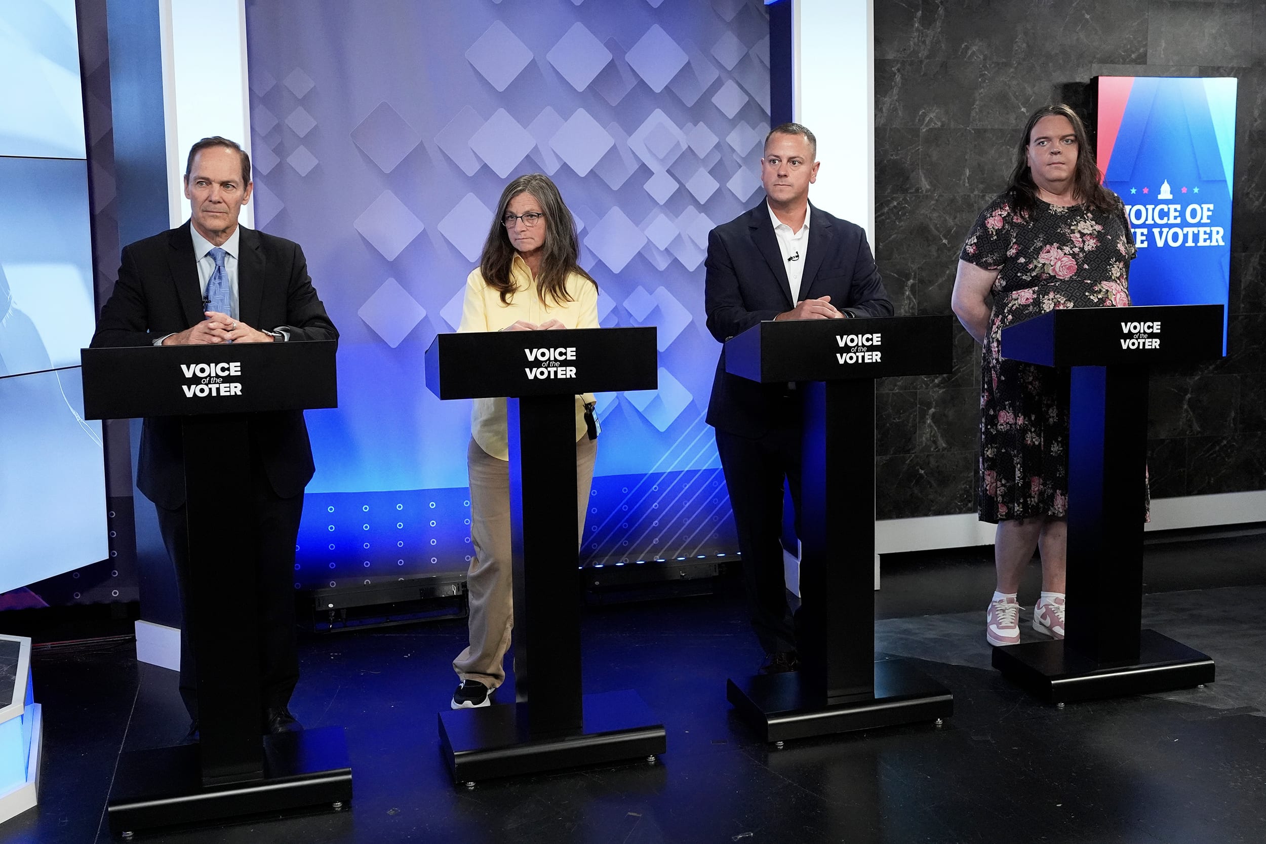 David Costello,Elizabeth Dickerson,Dan Kleban,Ashley Webb standing at a row of lecterns during a debate.