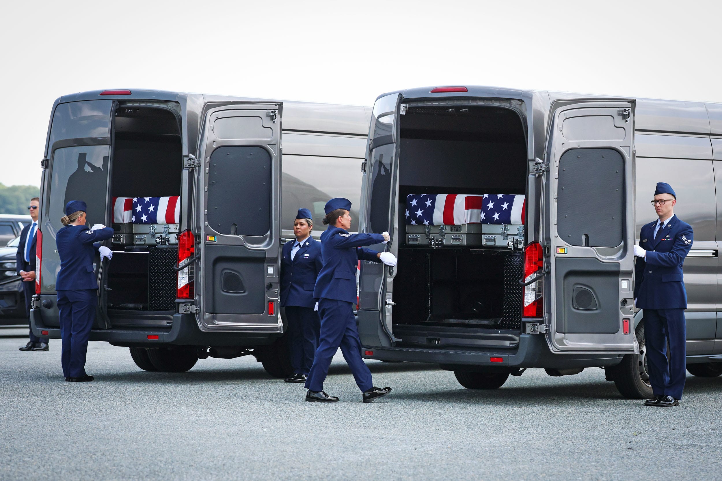 Flag-draped transfer cases are loaded into vehicles during a dignified transfer