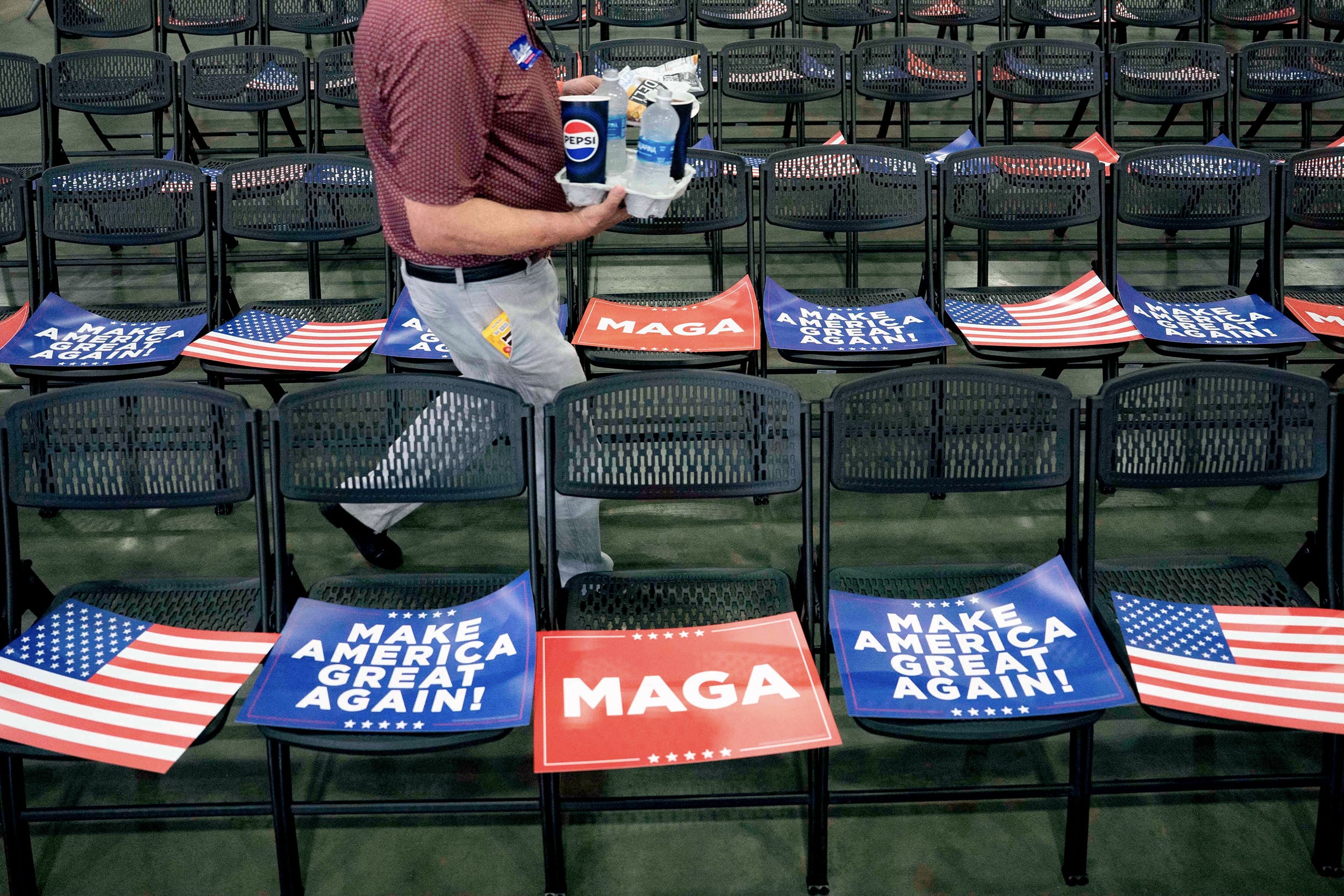 MAGA and American flag posters on folding chairs during an indoor rally.