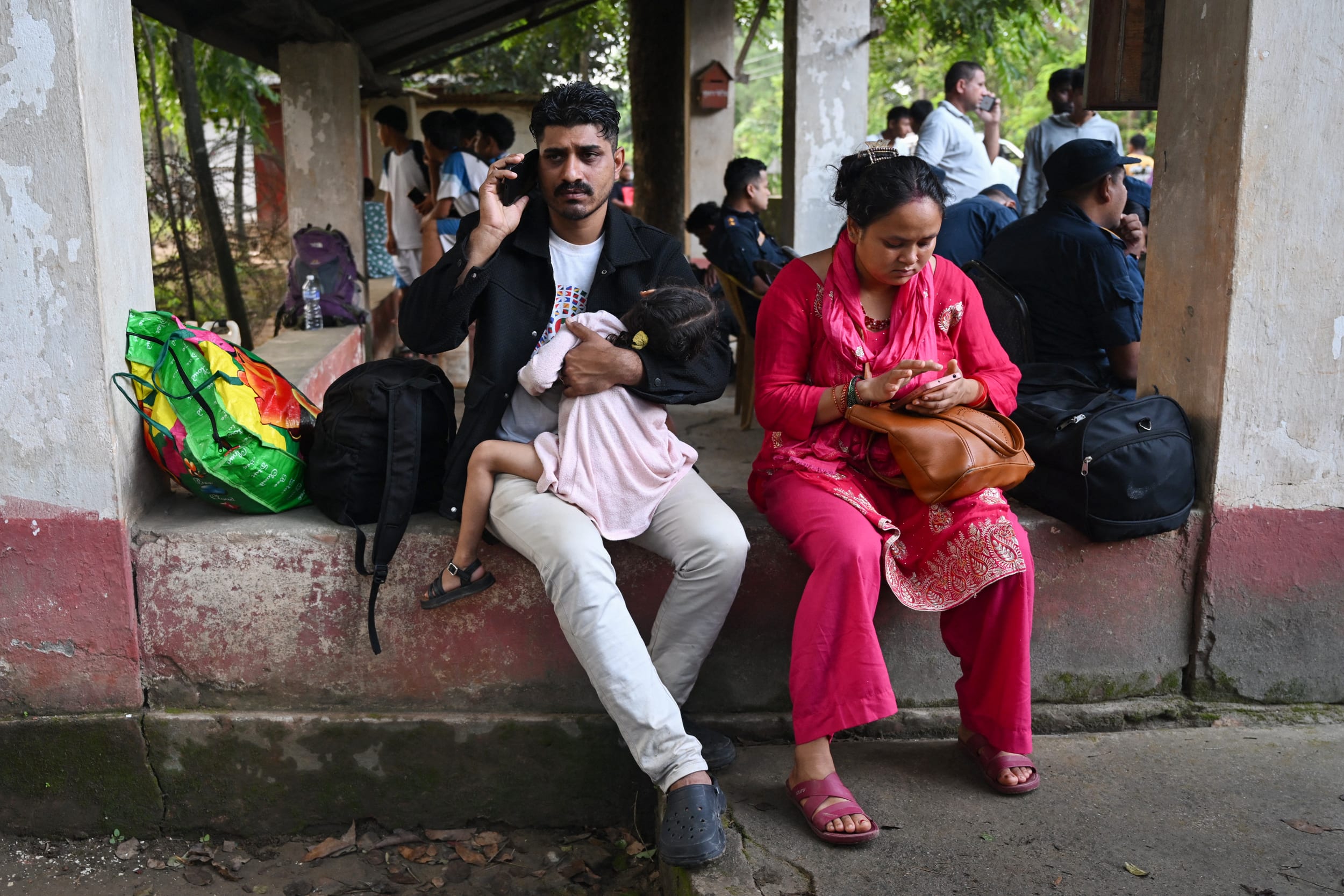From left, a man holds a toddler on his arms while he is on the phone; a woman appears to be browsing her phone.