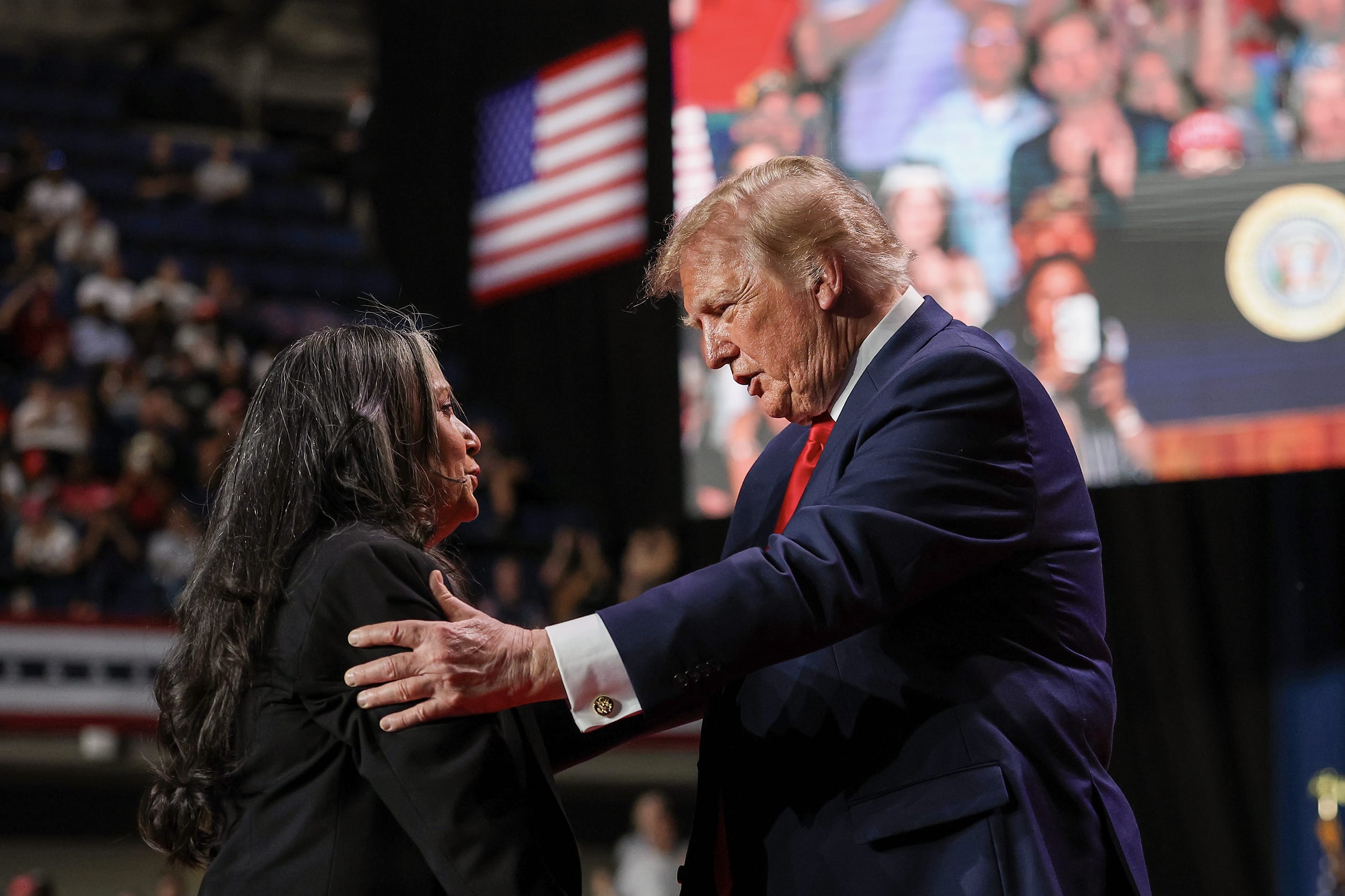 Donald Trump with both hands placed on the shoulders of a woman on stage during a rally.