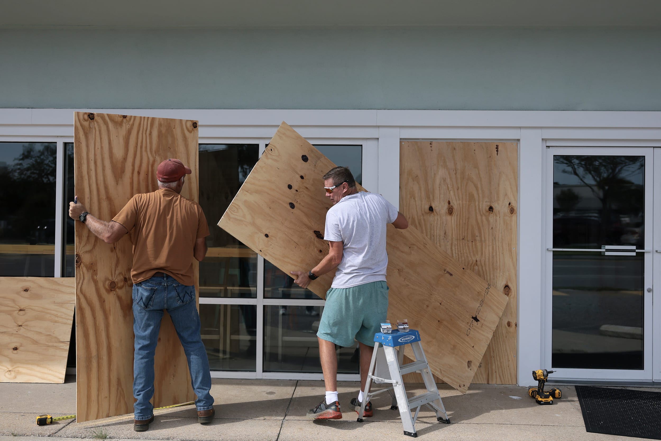 Two men work to place plywood over windows on a commercial building.