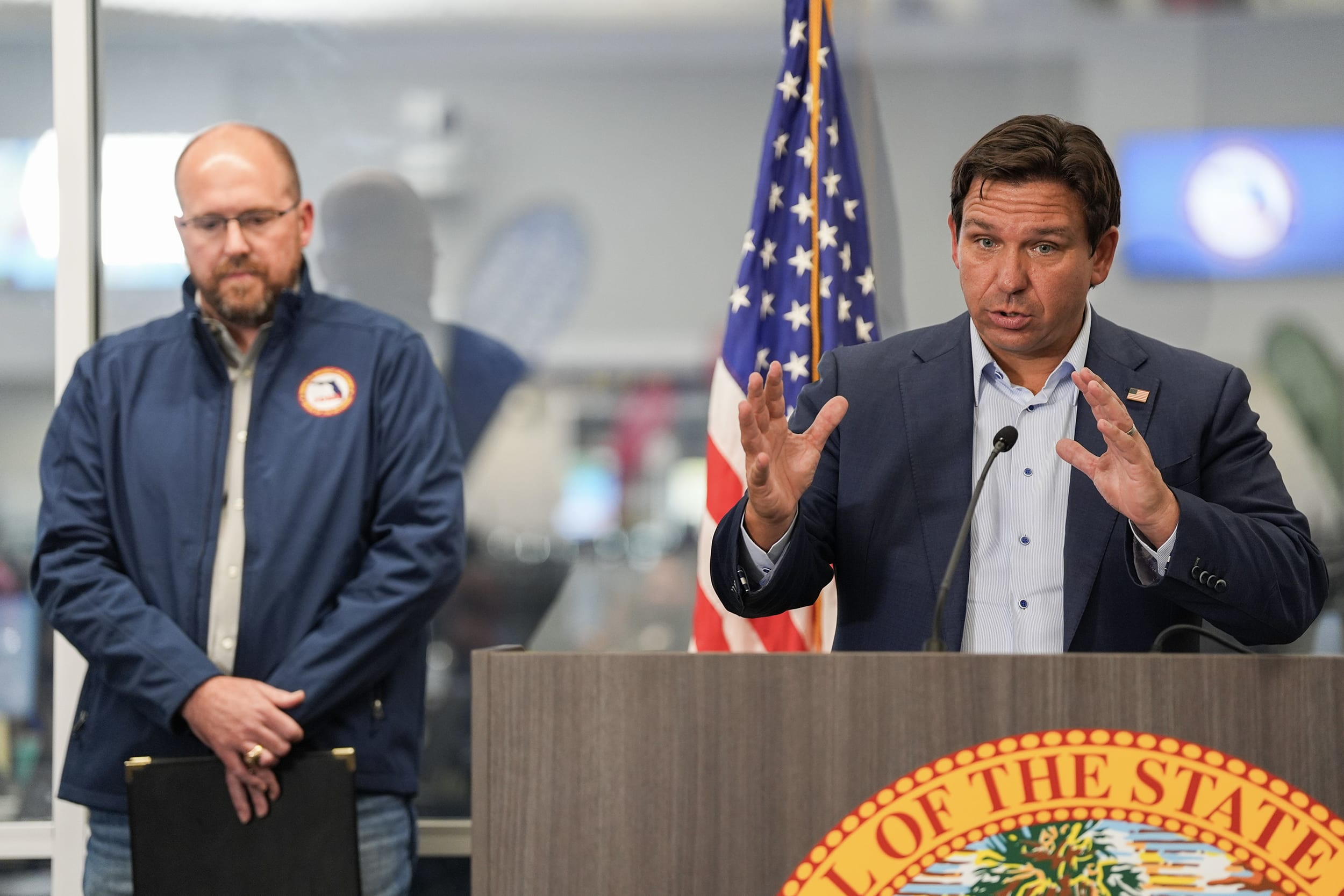 Ron DeSantis gestures with both hands while speaking at a podium during a press conference.