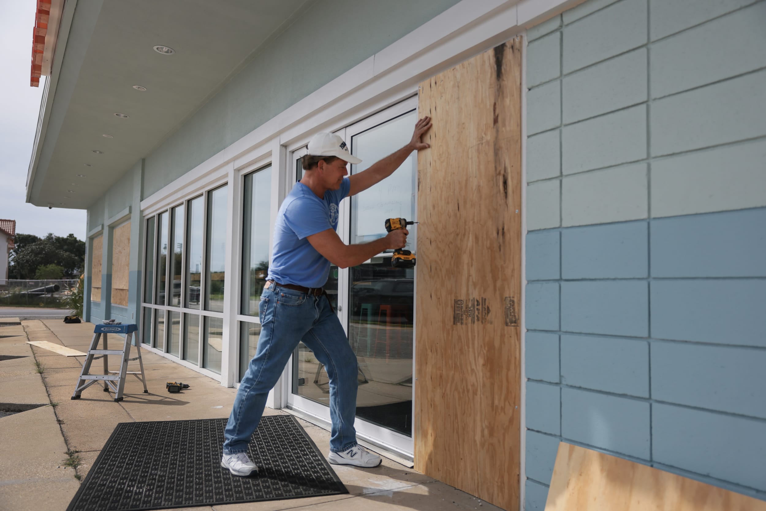 A man places plywood over the windows of a restaurant.