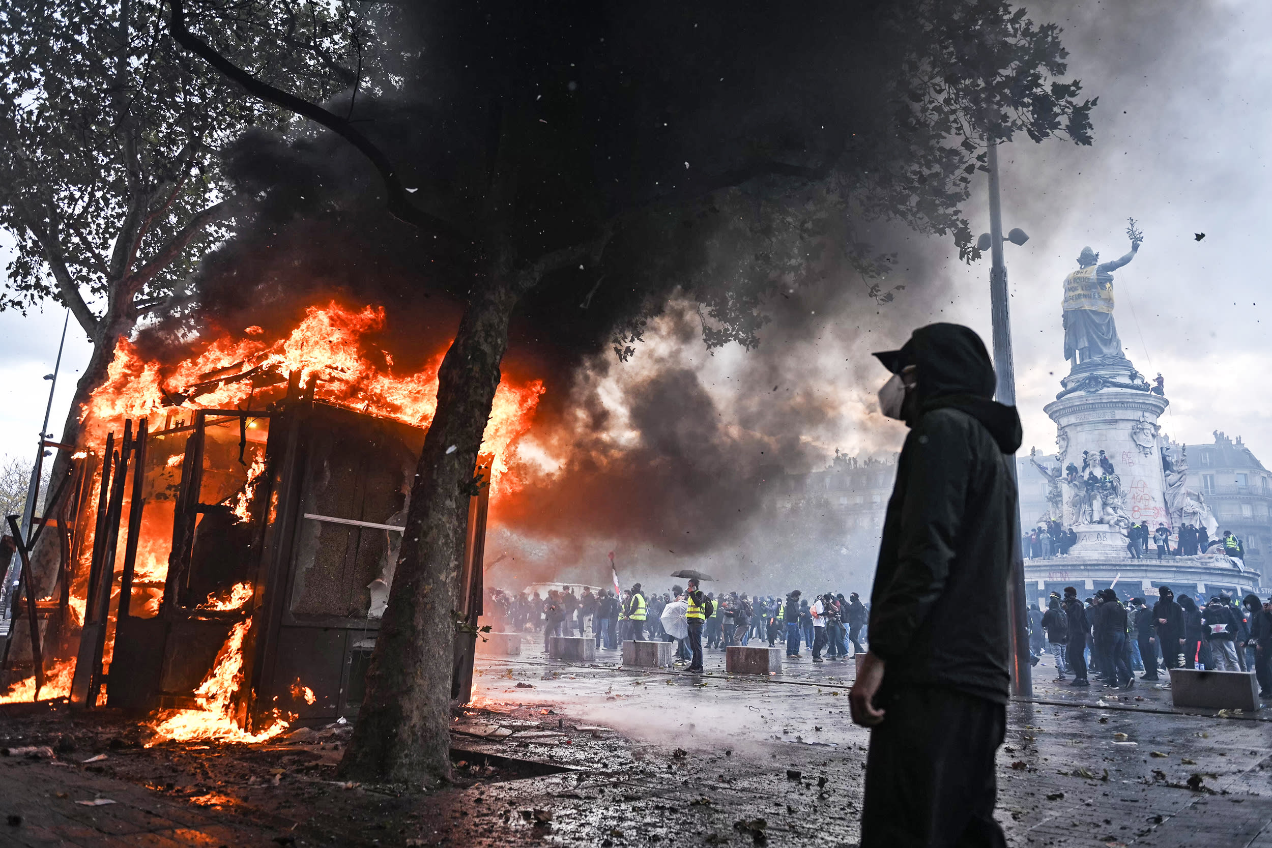 Image: A protester in Paris looks at a burning stand.